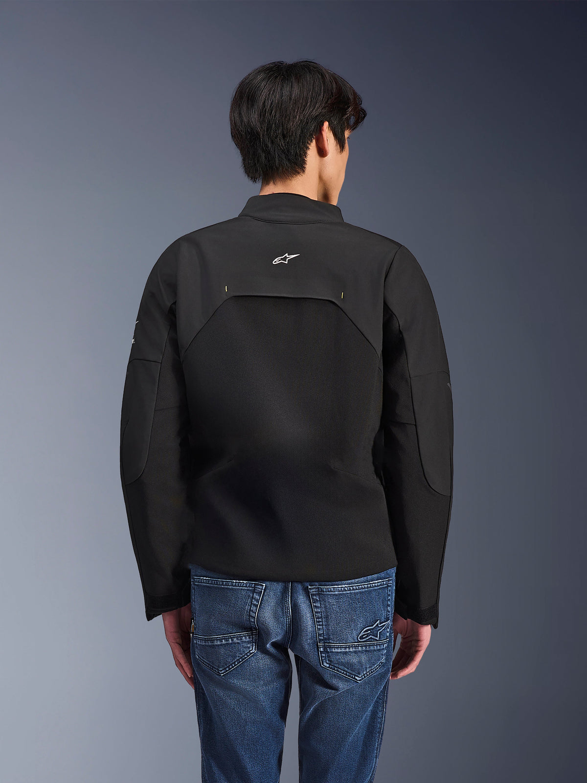 Giacca Alpinestars Provoke, giacca da moto urbana, nero, vista posteriore con logo Astars bianco e pannelli tecnici in ripstop, indossata con jeans in denim blu, design contemporaneo per il commuting cittadino