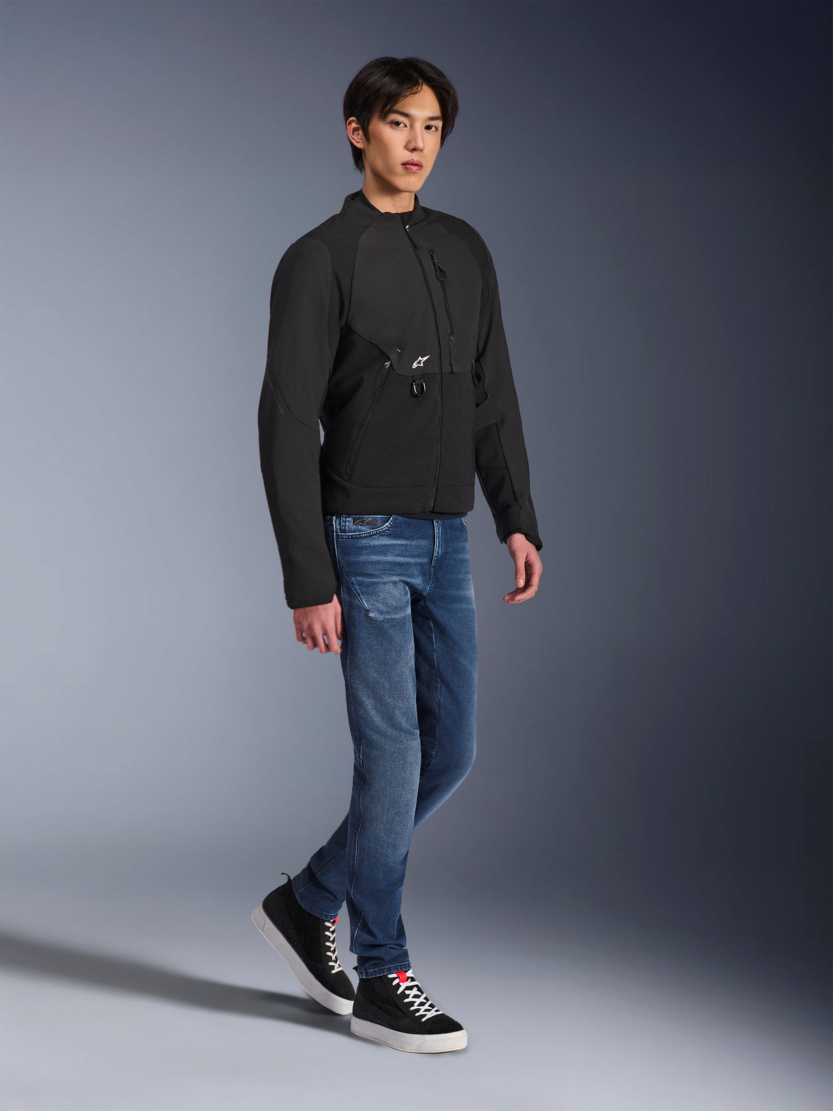 Giacca Alpinestars Provoke, giacca da moto urbana, nero, indossata da un modello con jeans blu e sneakers nere, design tecnico in tessuto con piccolo logo Alpinestars, scatto lifestyle a figura intera per la guida urbana contemporanea
