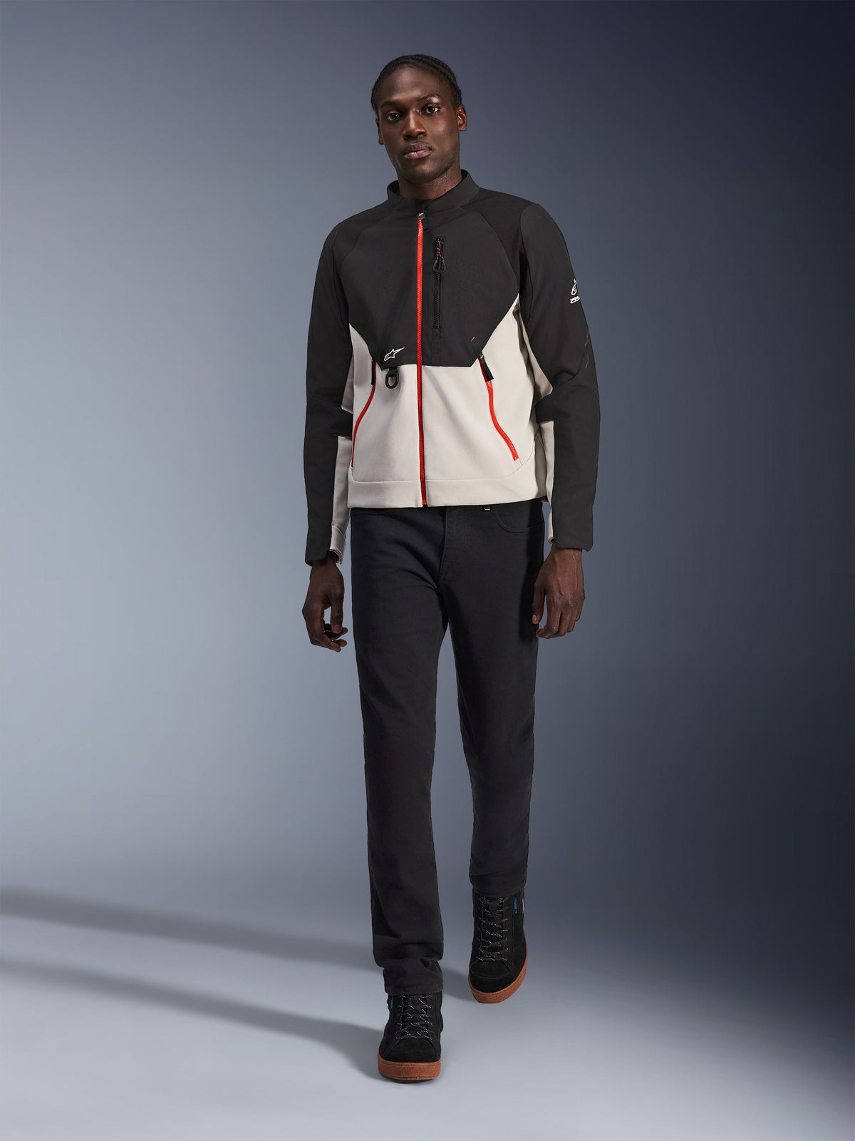 Modello che indossa la giacca Alpinestars Provoke, giacca da moto urbana in nero e grigio metallo con dettagli delle zip rossi, abbinata a pantaloni neri e scarpe alte nere, abbigliamento protettivo moderno per la guida urbana