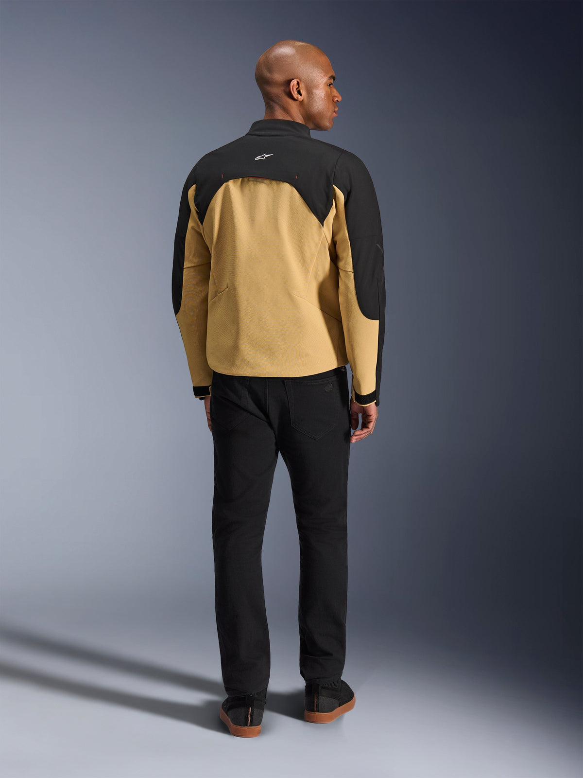 Giacca Alpinestars Provoke, Black e Camel, vista posteriore di giacca da moto urbana con carré superiore nero e parte inferiore della schiena color cammello, indossata da un modello con pantaloni neri, design contemporaneo ispirato allo streetwear