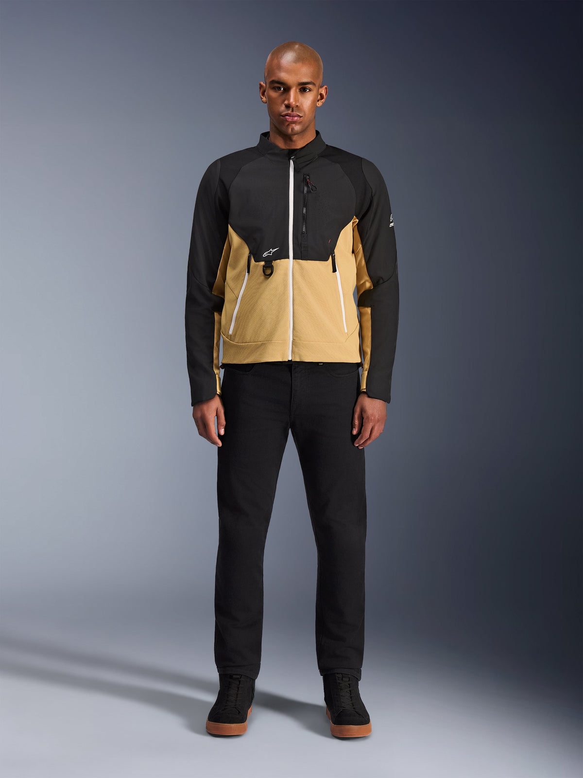Giacca Alpinestars Provoke in Black Camel, giacca da moto urbana caratterizzata da un design bicolore nero e cammello, indossata da un modello con pantaloni neri e scarpe nere, silhouette contemporanea con cerniere bianche e costruzione in softshell tecnico.