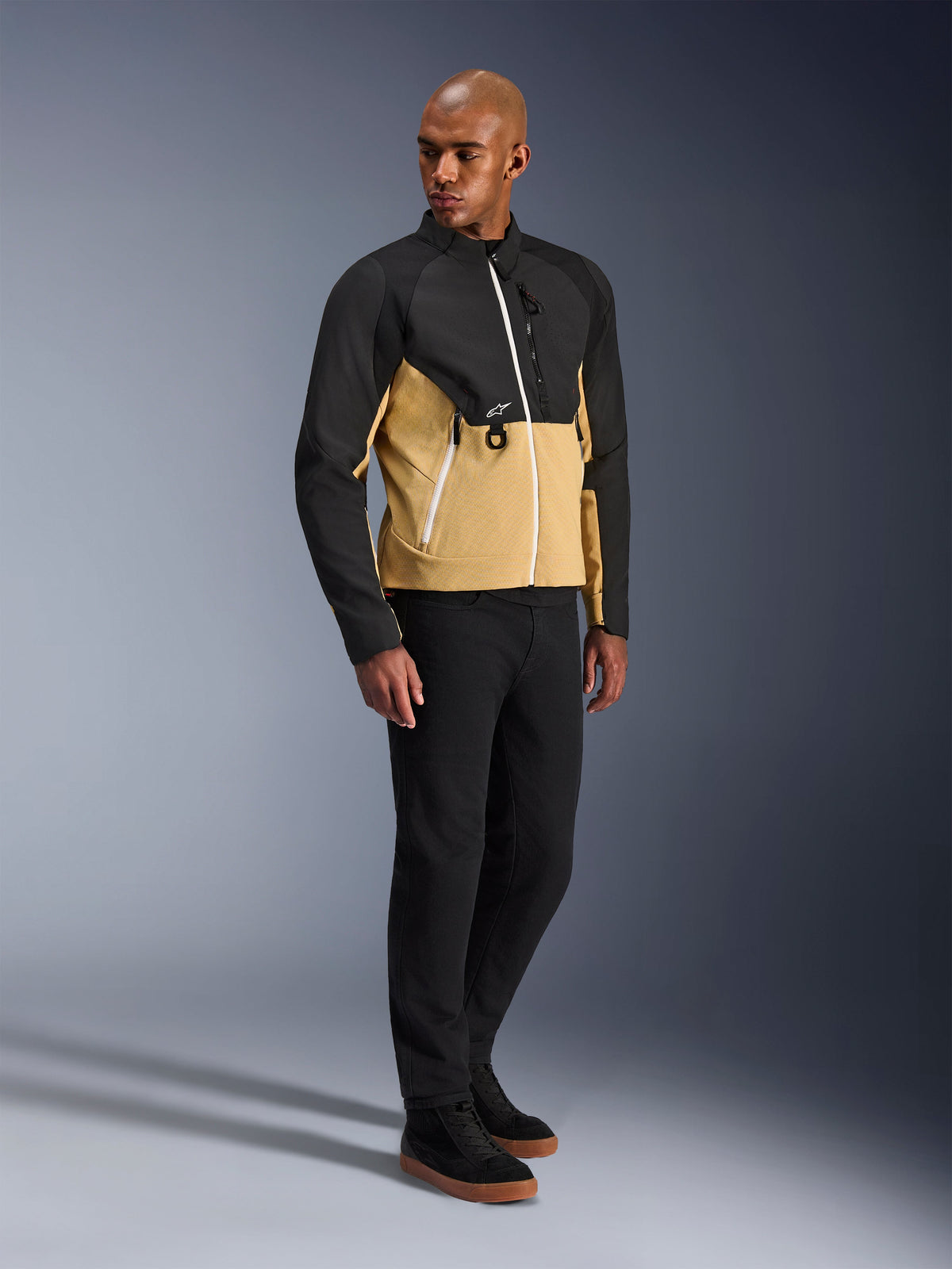 Giacca Alpinestars Provoke, giacca da moto urbana, Black Camel, indossata da un modello con pantaloni neri e sneakers, design bicolore in tessuto con parte superiore nera e parte inferiore color cammello, dettagli zip bianchi, abbigliamento da moto urbano contemporaneo