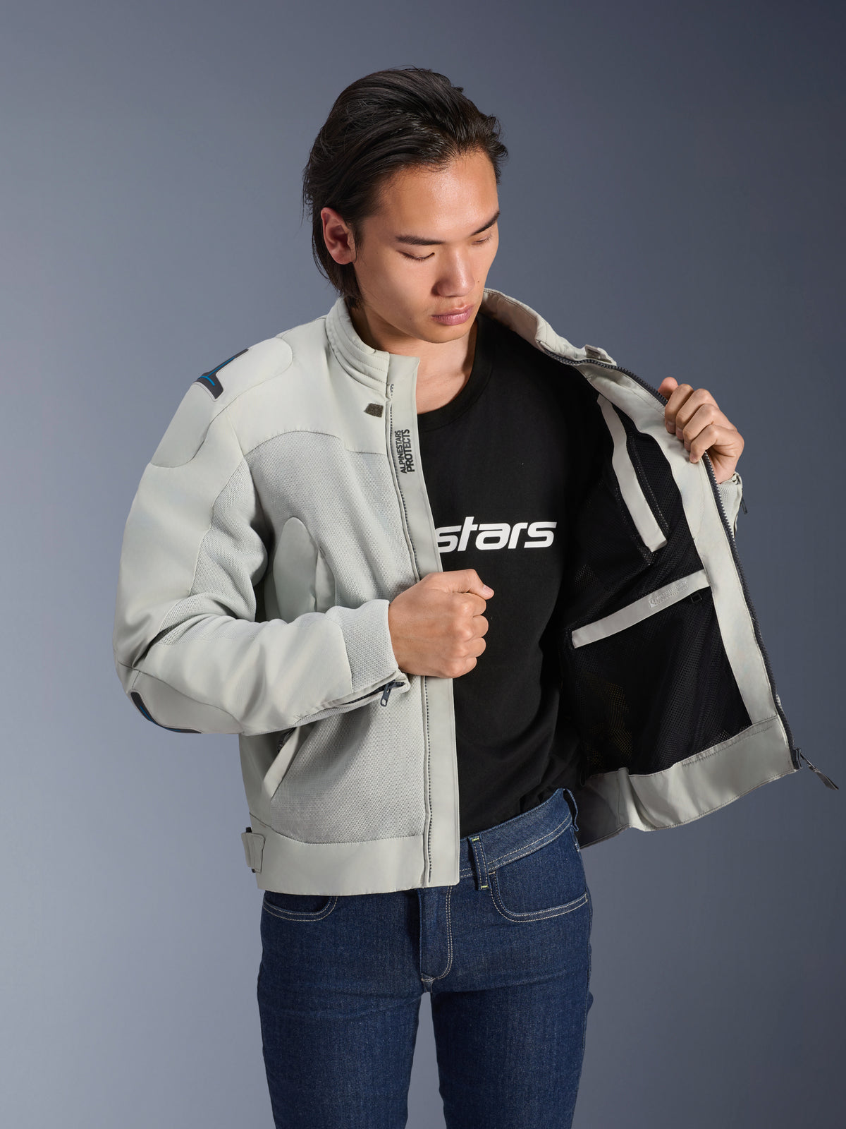 Giacca Alpinestars Circal-1 Air, Metal Gray, mostrata aperta per esporre la fodera interna in mesh e i dettagli delle tasche, indossata da un modello con t-shirt nera con logo e jeans blu, stile urban motorcycle