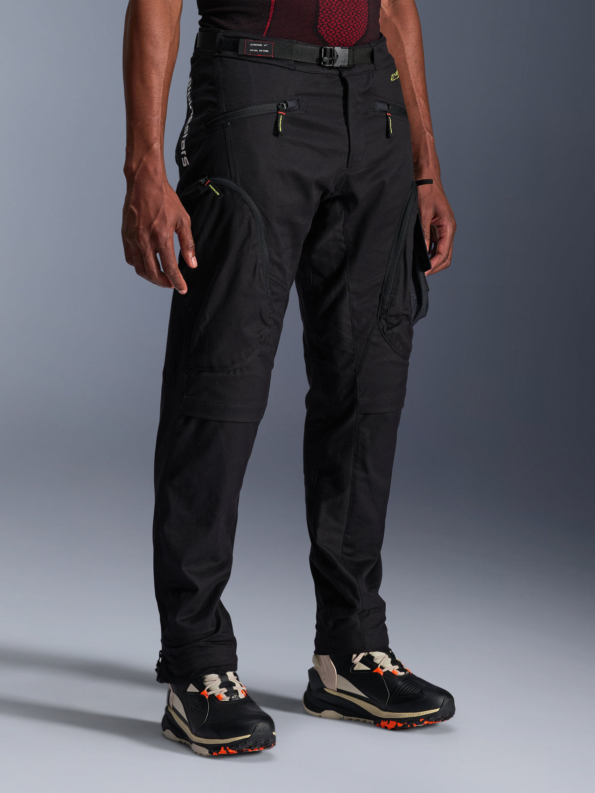 Pantaloni Alpinestars Acteon, pantaloni da moto neri, indossati da un modello, con silhouette moderna affusolata, tasche cargo con zip, cintura regolabile in vita e sneakers tecniche, abbigliamento da moto urbano