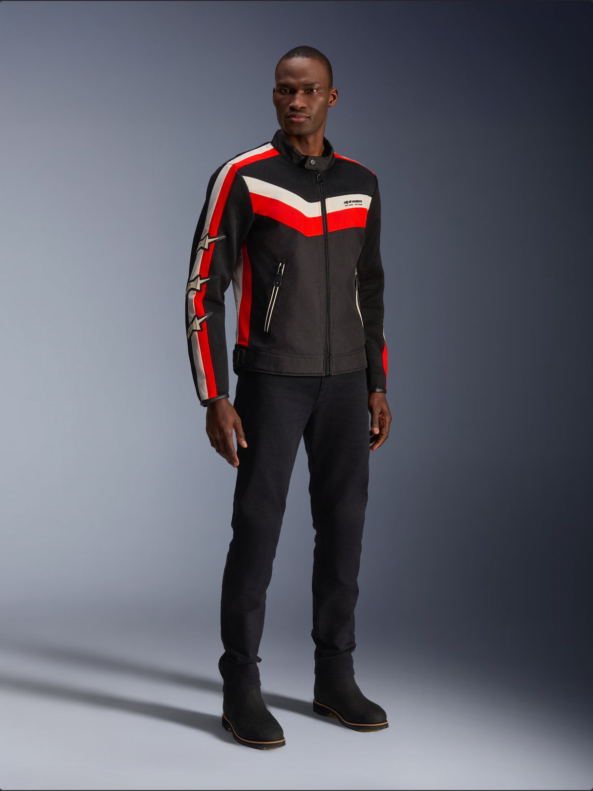 Alpinestars T-Dyno Air Jacket, Nero Rosso Brillante Ecru, giacca da moto in tessuto da uomo con pannelli in mesh 3D, con strisce a scaglioni rosse e bianche sul petto e loghi a stella sulle maniche, indossata da un modello con pantaloni e stivali neri.