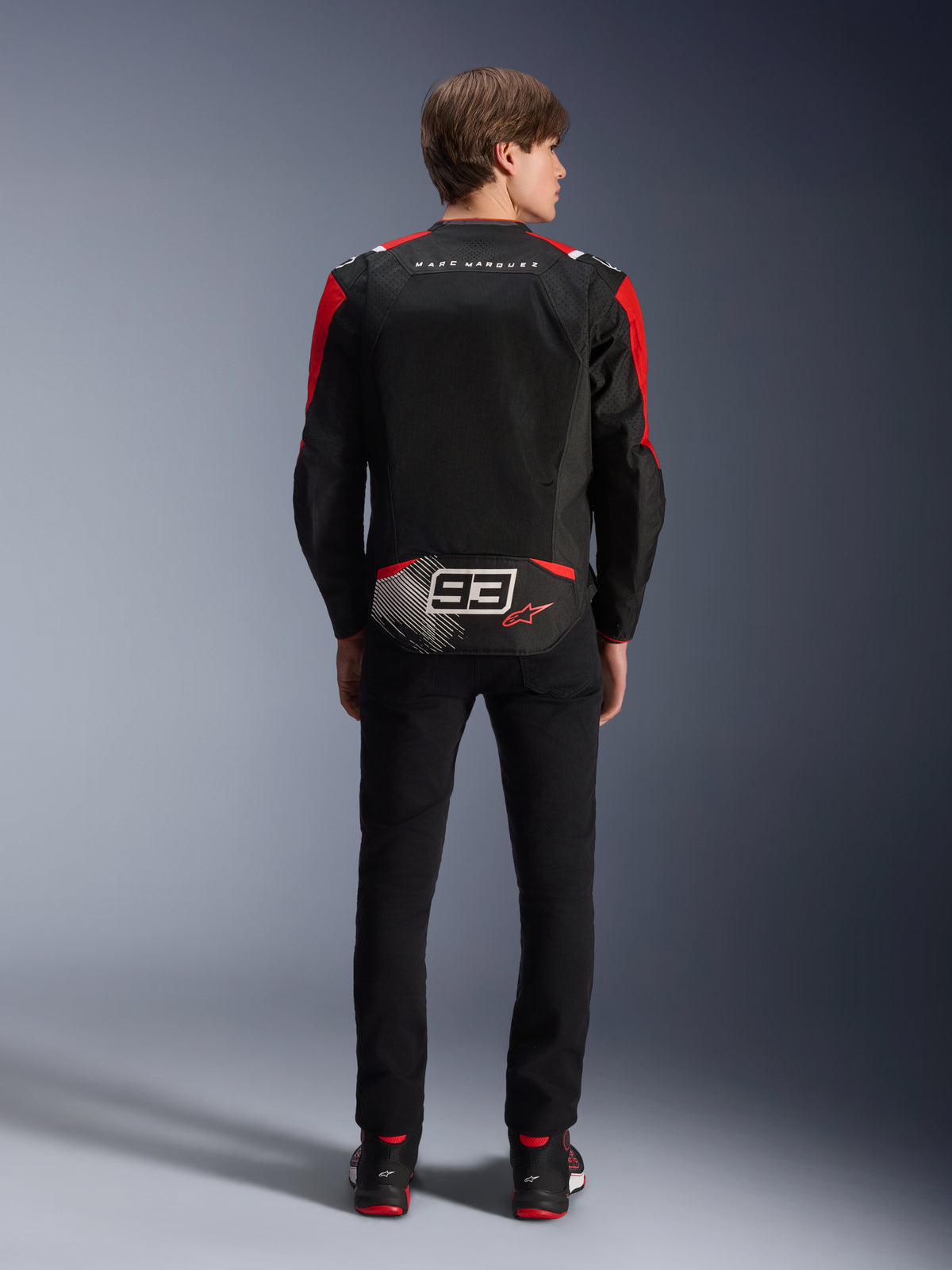 Giacca Alpinestars MM93 T-SPS Air V2, vista posteriore su modello, nera con accenti rosso brillante e bianchi, con firma Marc Marquez e logo 93 sulla schiena, giacca da moto tecnica in tessuto per uso urbano