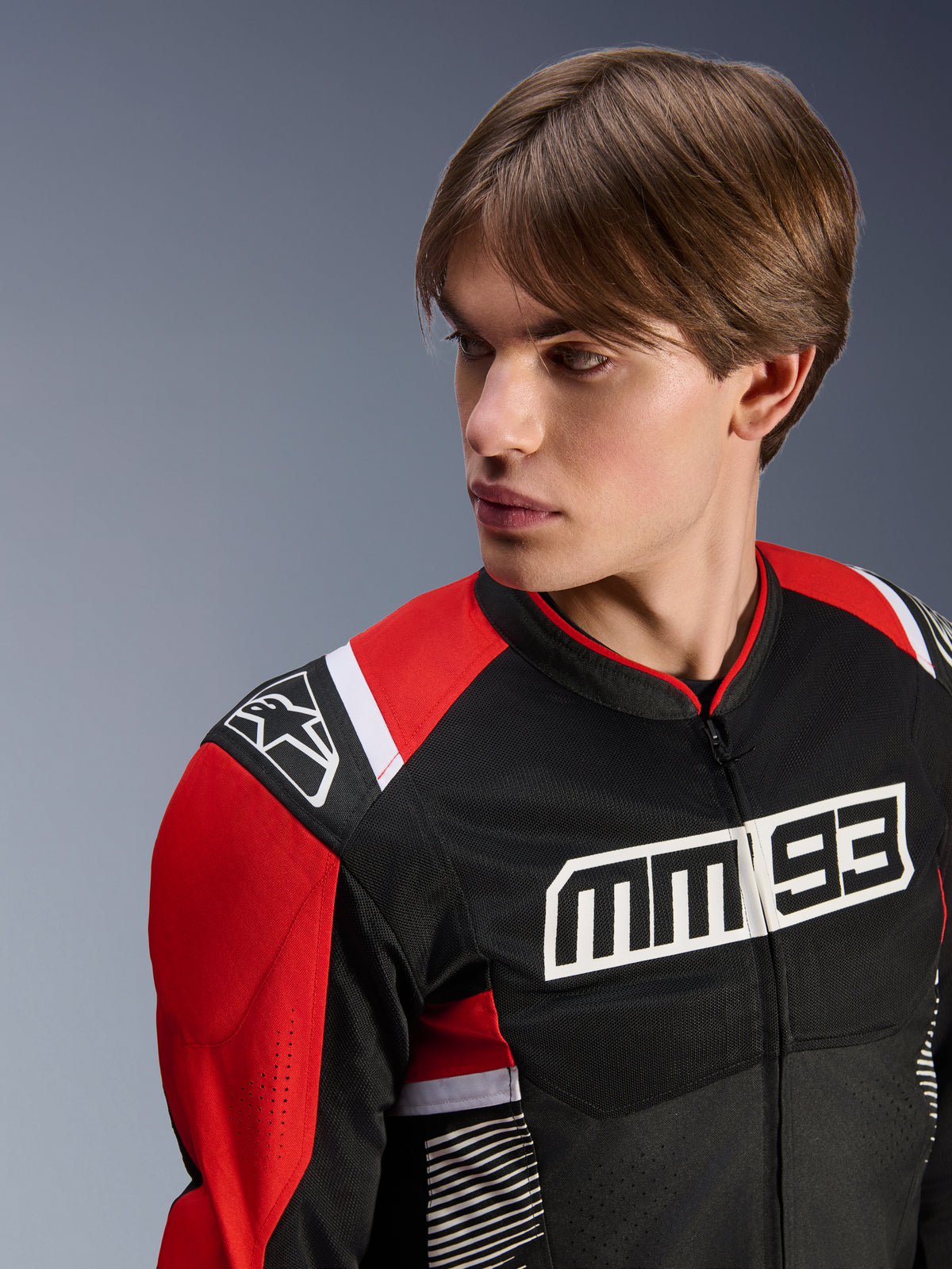 Modello che indossa la giacca Alpinestars MM93 T-SPS Air V2, giacca da moto in tessuto, nero, rosso brillante e bianco, con logo MM 93 sul petto e logo a stella sulla spalla, struttura in mesh per la ventilazione, abbigliamento tecnico sportivo