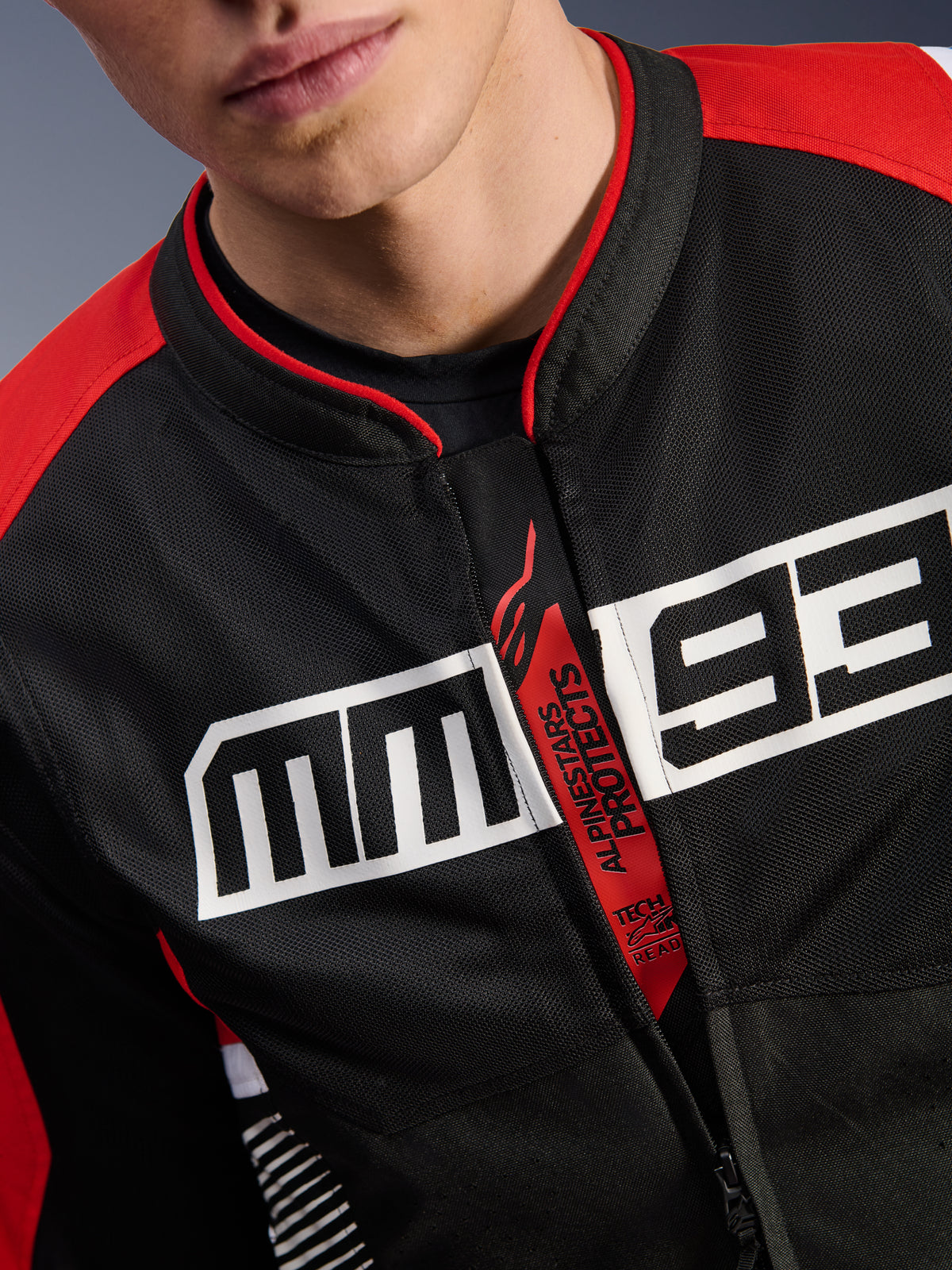Alpinestars MM93 T-SPS Air V2 Jacket, giacca da moto, nero, rosso brillante e bianco, primo piano del petto con grande logo MM93 bianco, tiretto della cerniera rosso 'Alpinestars Protects' e 'Tech-Air Ready', trama in tessuto mesh tecnico