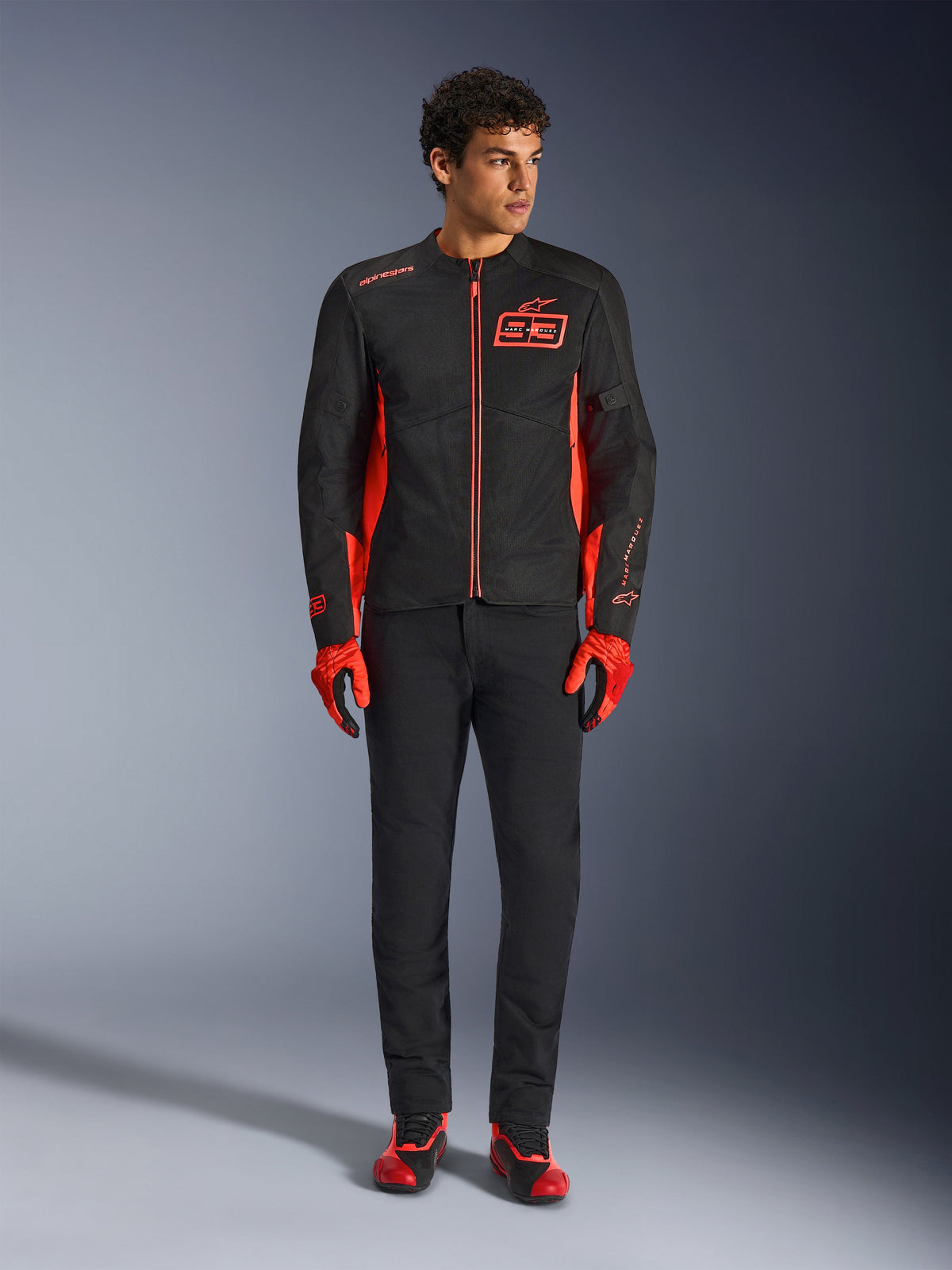 Alpinestars MM93 C-1 Air Jacket, giacca da moto, nero e rosso fluo, con branding Marc Marquez e logo 93, indossata da un modello con guanti rossi abbinati e pantaloni neri, costruzione leggera in tessuto e mesh per la guida urbana