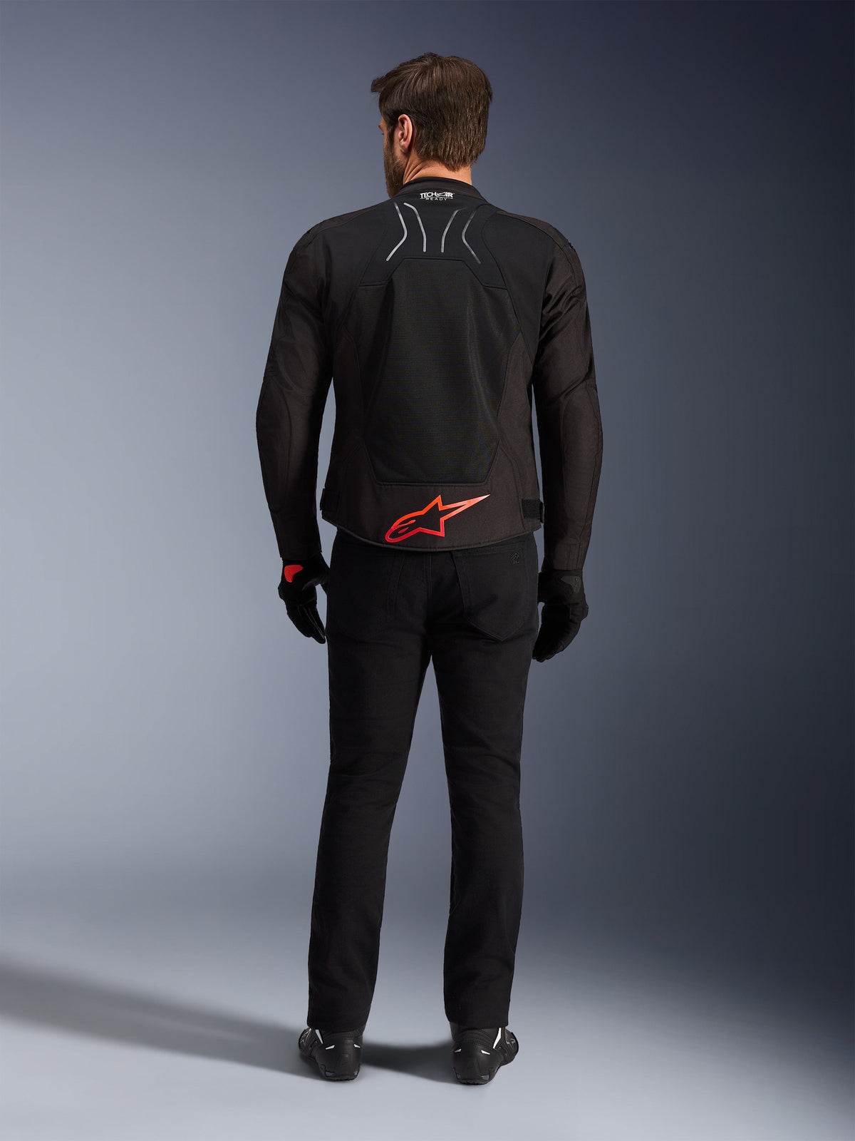 Giacca Alpinestars SMX Air, nera con logo Bright Red, vista posteriore che mostra il marchio Tech-Air Ready e i pannelli di ventilazione in mesh, indossata con pantaloni e guanti neri, abbigliamento moto sportivo e racing ad alte prestazioni