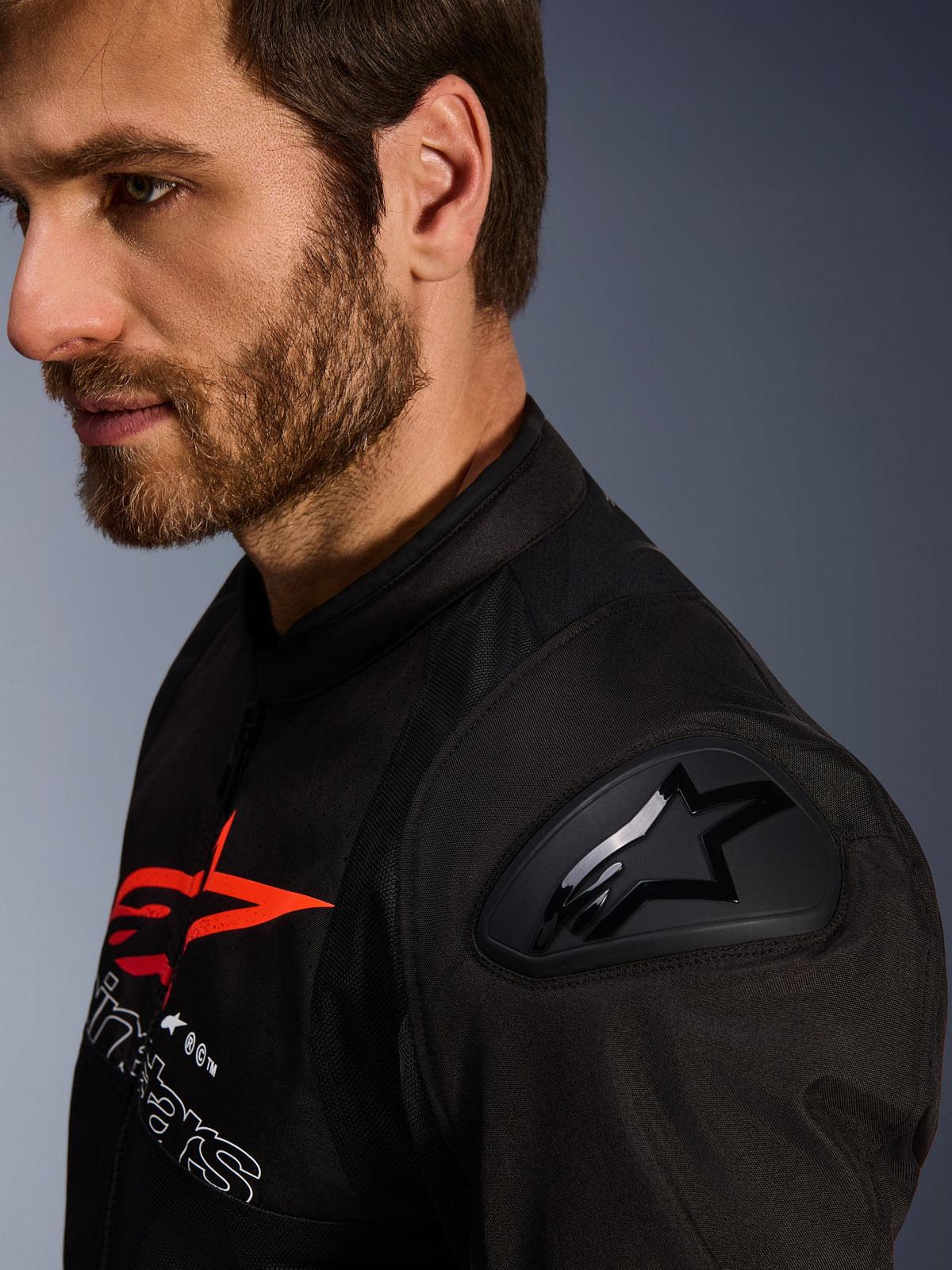 Giacca Alpinestars SMX Air, nero e rosso, dettaglio ravvicinato della protezione per spalle DFS Lite con logo a stella, indossata da un uomo con la barba, giacca da moto in tessuto per uso racing e sportivo