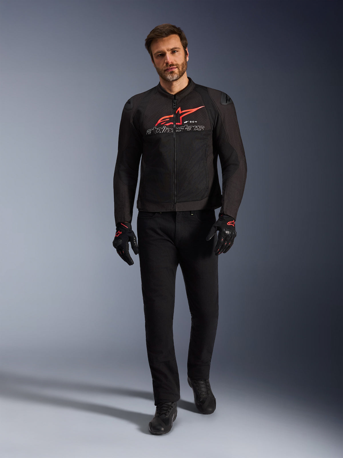 Giacca Alpinestars SMX Air, nero, rosso brillante e bianco, giacca da moto sportiva indossata con pantaloni da guida e guanti neri, con pannelli in rete tecnica e un vistoso logo Alpinestars rosso sul petto, outfit da strada ad alte prestazioni