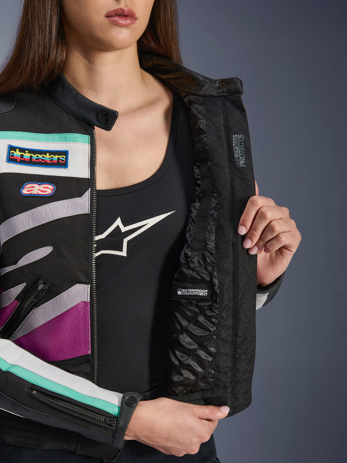 Giacca da donna Alpinestars Idles, Nero Bianco Sporco Viola, vista ravvicinata della fodera interna trapuntata con scomparto impermeabile, toppe da corsa d'ispirazione vintage e accenti color foglia di tè e viola sull'esterno in tessuto.
