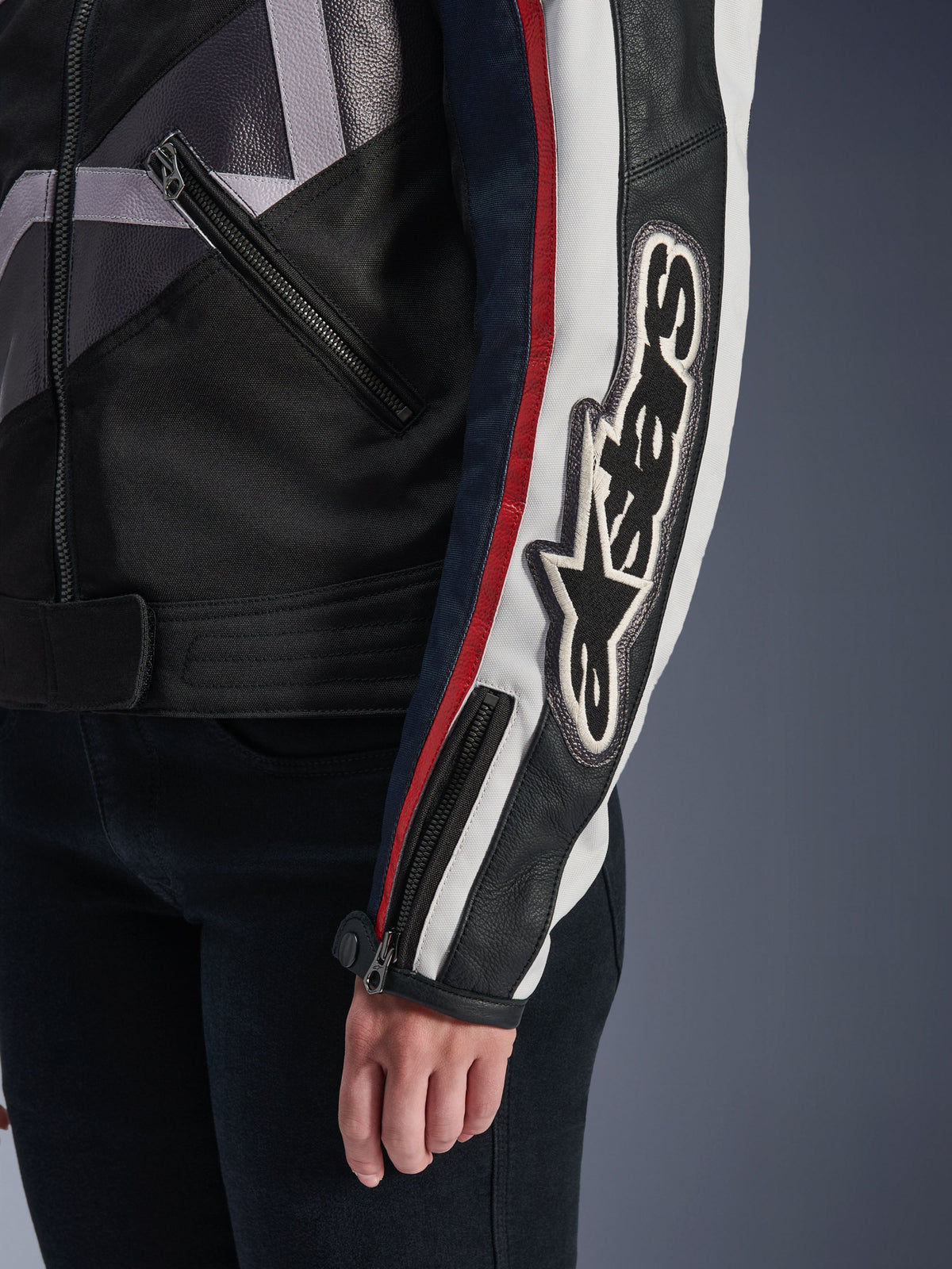 Giacca da donna Alpinestars Idles, giacca da moto urban, Off White Flame Red Black, primo piano della manica con grande logo Alpinestars ricamato, strisce racing rosse e bianche, costruzione in tessuto e pelle nera, dettagli con cerniere in metallo.