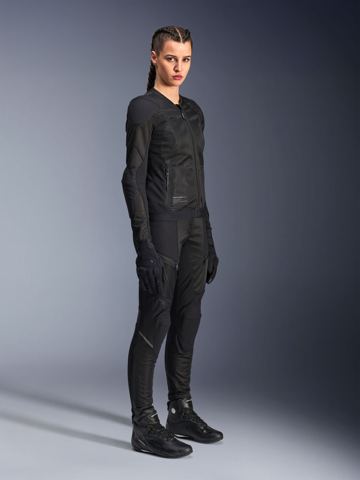 Motociclista donna che indossa la giacca Alpinestars Stella Troop-Air in nero, caratterizzata da una costruzione in mesh tecnico 2D, abbinata a pantaloni, guanti e stivali da moto neri coordinati, in stile urban riding.