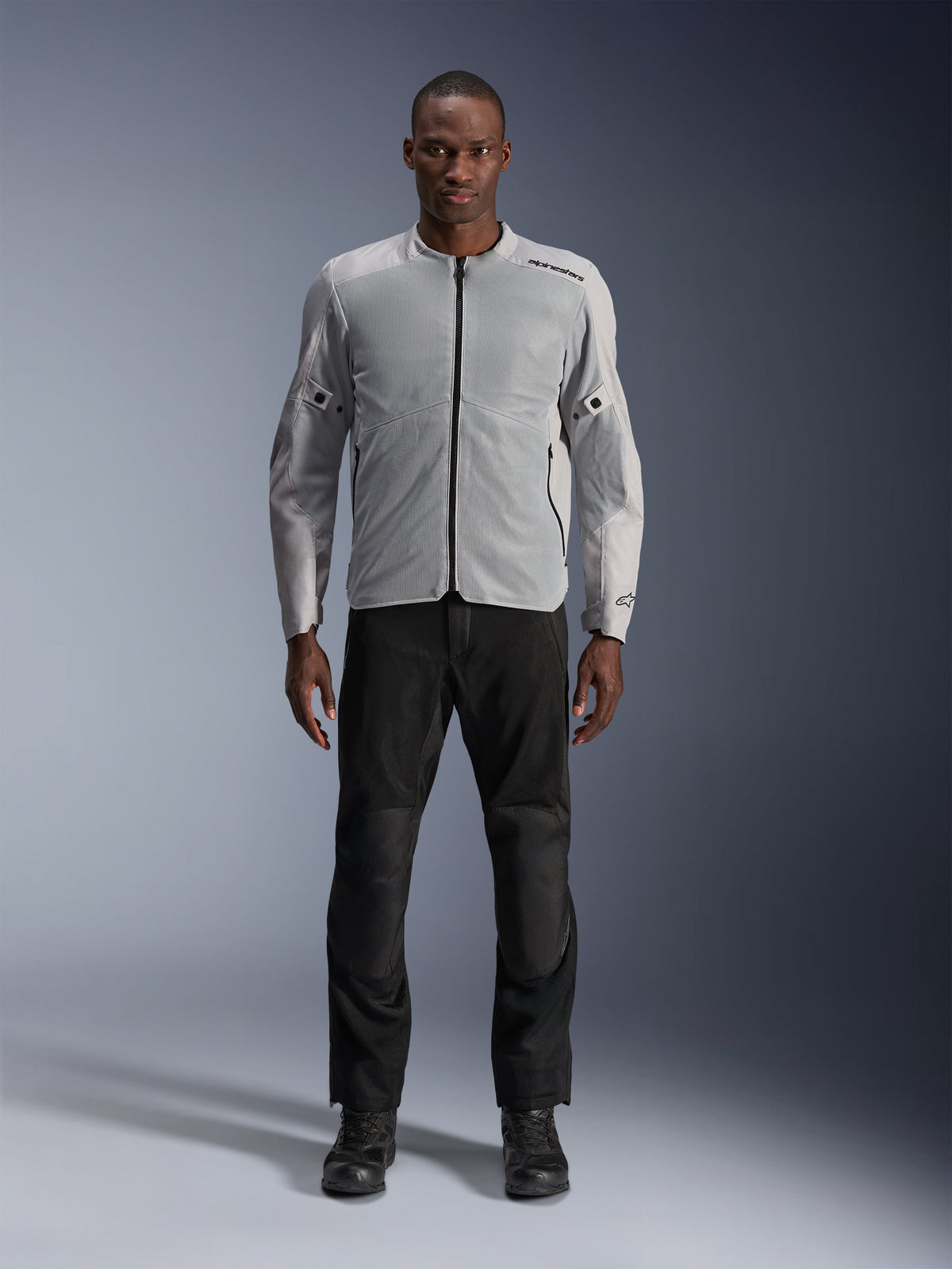 Giacca Alpinestars C-1 Air in Silver, giacca da moto urban in tessuto da uomo con pannelli in rete ventilata, indossata da un modello con pantaloni da guida neri e stivali neri, stile commuting contemporaneo