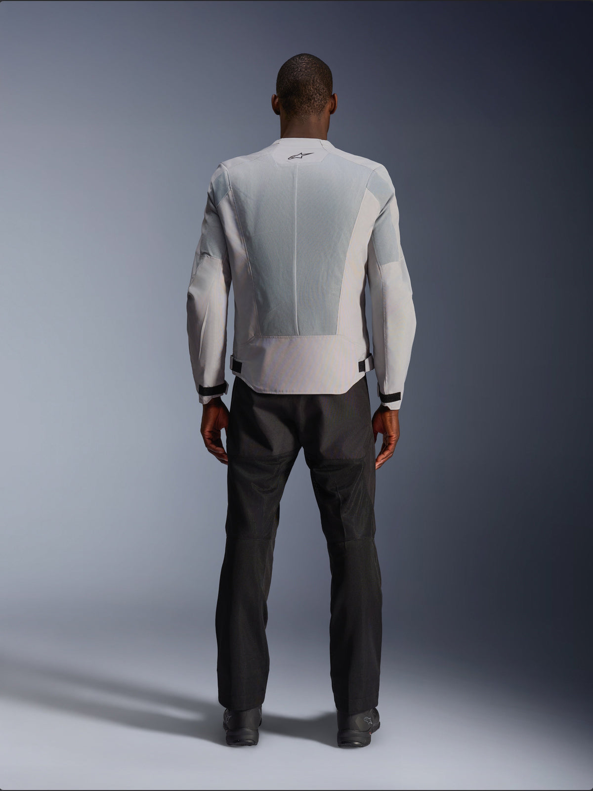 Giacca Alpinestars C-1 Air in Silver, vista dal retro su un modello maschile, giacca da moto in tessuto con ampi pannelli di ventilazione in mesh tecnico, piccolo logo nero sul collo e regolatori in vita, indossata con pantaloni da guida neri per un look urban contemporary.