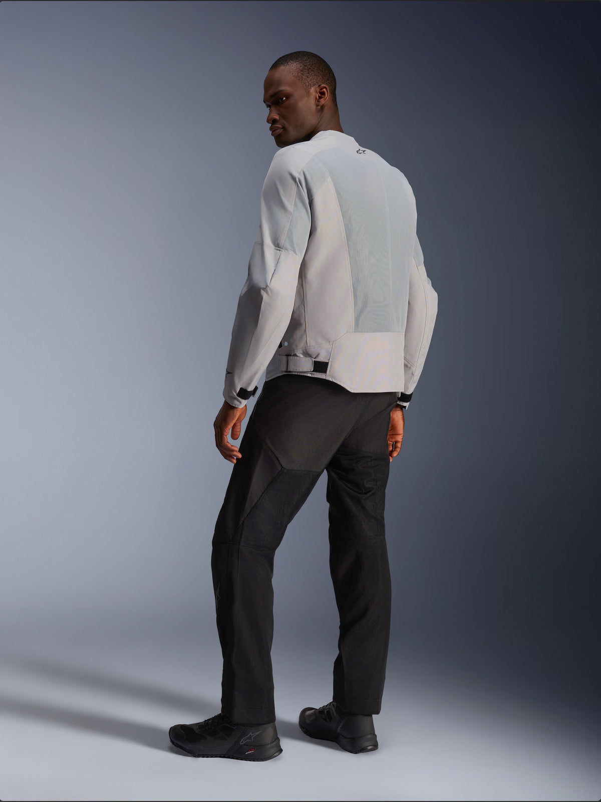 Giacca Alpinestars C-1 Air, argento e grigio, vista dal retro su un modello, con pannelli in mesh tecnico ventilato e loghi riflettenti, indossata con pantaloni e scarpe neri, abbigliamento da moto urban contemporary.