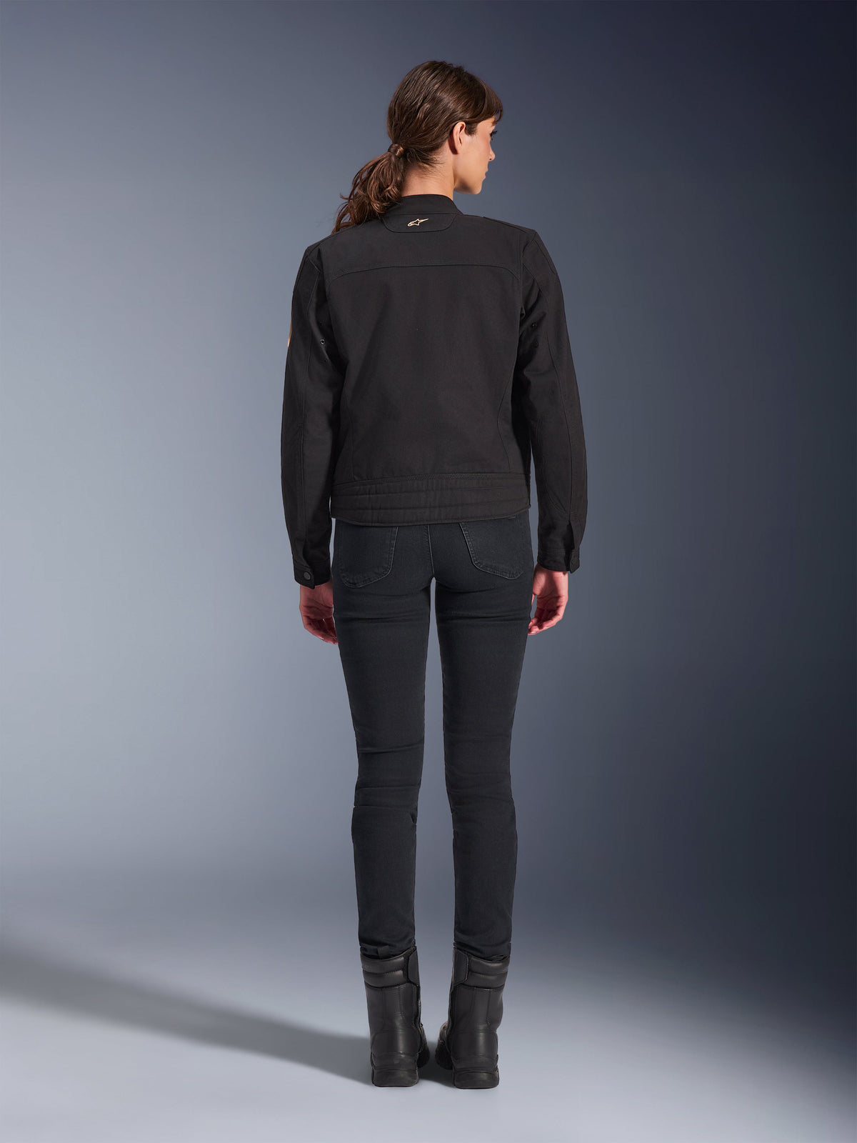 Giacca Alpinestars Stella Grace, giacca da moto urban da donna, nero, vista posteriore con design ispirato al workwear, indossata con pantaloni neri slim-fit e stivali neri, scatto in studio