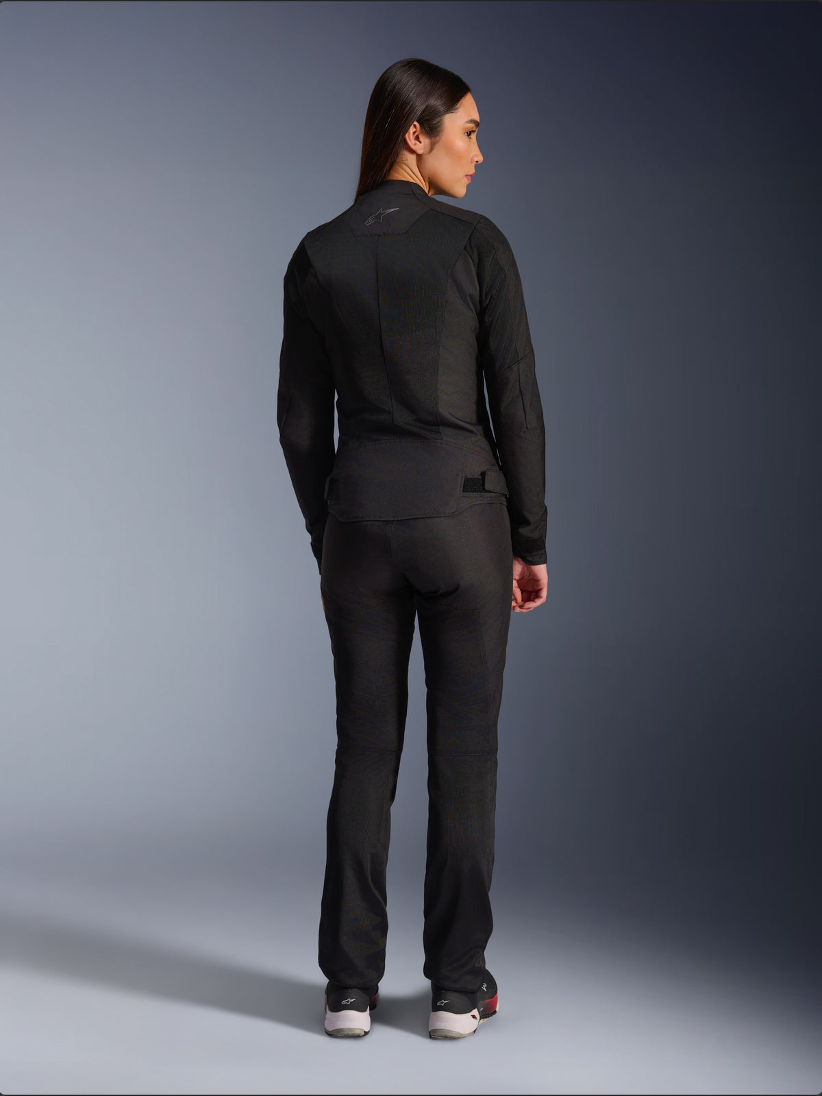 Giacca Alpinestars Stella C-1 Air, giacca da moto in tessuto per donna, nera, vista posteriore che mostra la costruzione in mesh e il logo discreto sulla parte superiore della schiena, indossata con pantaloni da moto neri coordinati, stile urban contemporaneo.
