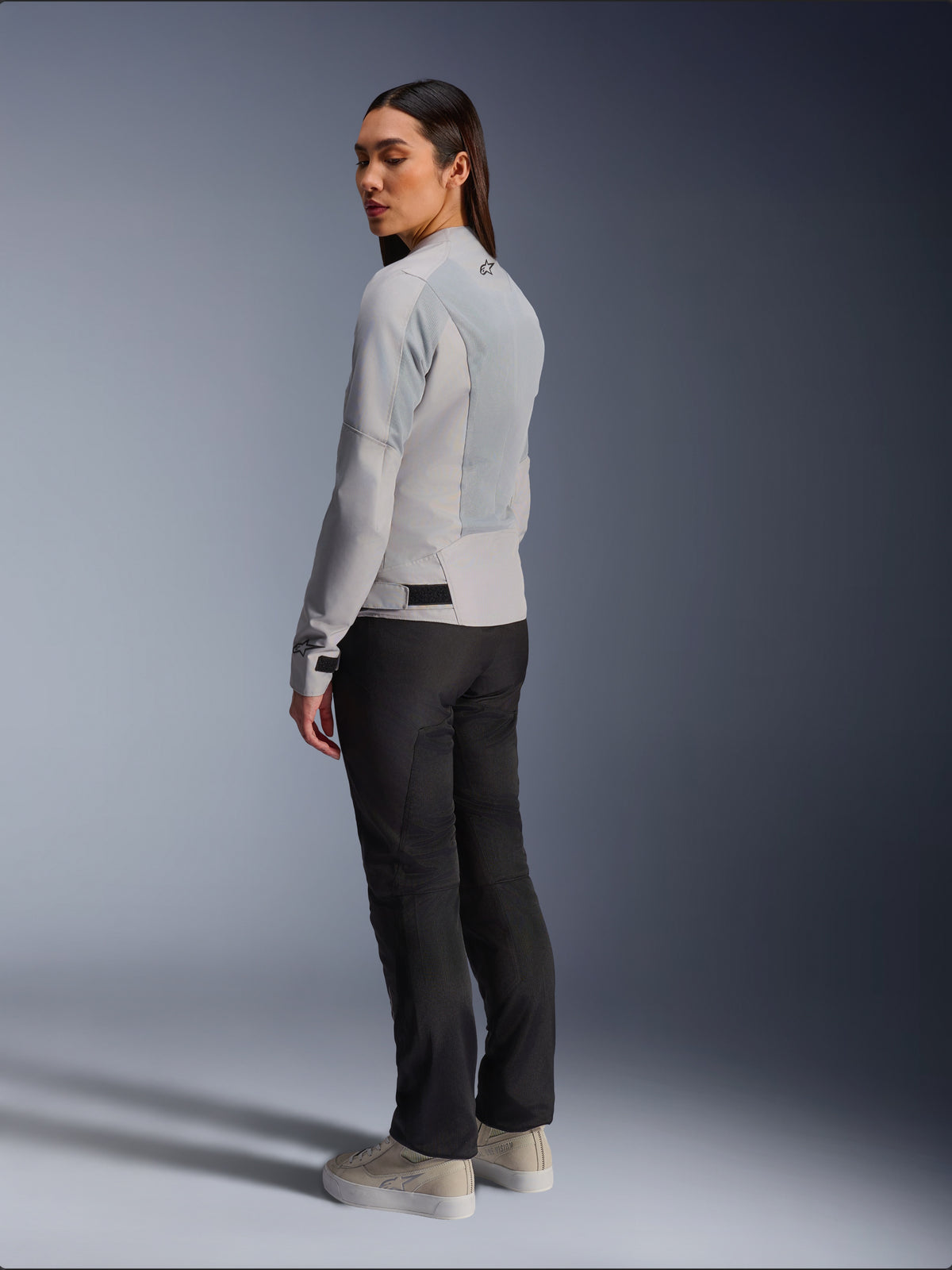 Donna che indossa la giacca Alpinestars Stella C-1 Air in Silver, vista posteriore e laterale che mostra i pannelli in rete tecnica e il logo riflettente sulla spalla, abbinata a pantaloni da moto neri e sneaker beige, estetica urban riding contemporanea