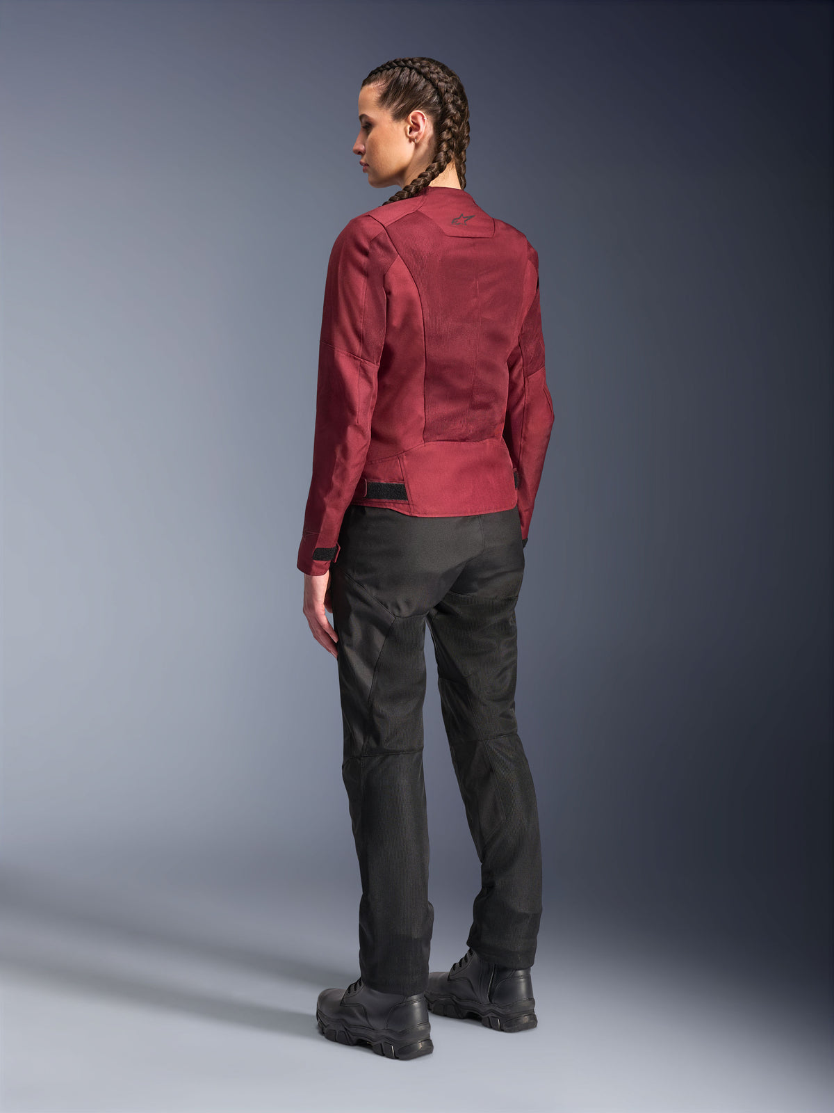 Motociclista che indossa la giacca Alpinestars Stella C-1 Air bordeaux e i pantaloni Stella C-1 Air neri, vista posteriore a figura intera, abbigliamento da moto urbano con pannelli in mesh tecnico, abbinato a stivali da moto neri