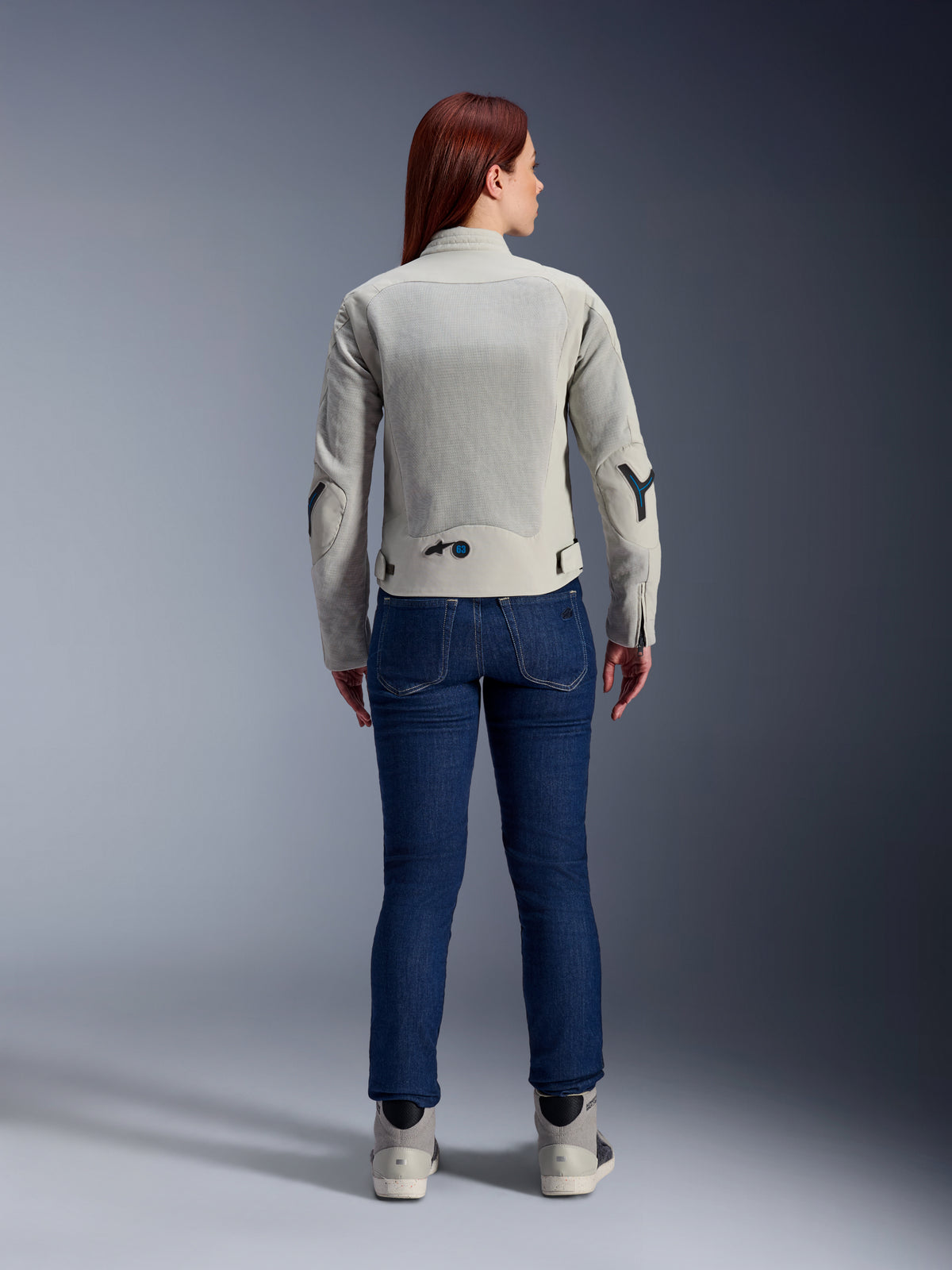 Giacca Alpinestars Stella Circal-1 Air da donna in grigio metallo e blu metile, vista posteriore, con ampi pannelli in rete per il flusso d'aria su schiena e braccia, indossata con jeans in denim blu scuro e scarpe da moto grigie per un look urban moderno.