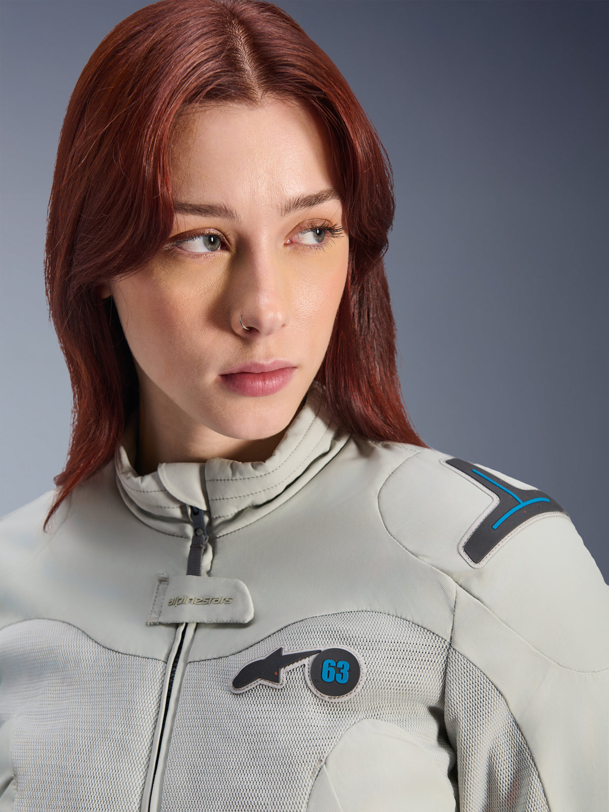 Donna che indossa la giacca Alpinestars Stella Circal-1 Air, giacca da moto in tessuto da donna, grigio metallo e blu metile, scatto lifestyle in primo piano con pannelli in rete per il flusso d'aria, colletto imbottito e toppa con logo Alpinestars con il numero 63.