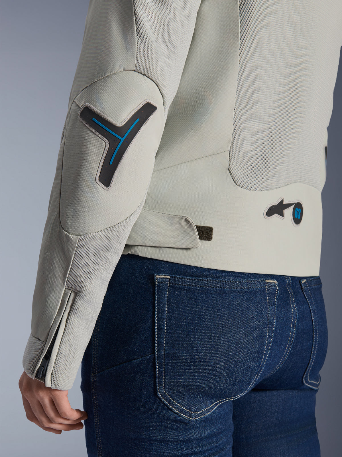 Giacca da donna Alpinestars Stella Circal-1 Air, grigio Metal Gray e blu Methyl Blue, dettaglio ravvicinato di schiena e manica con pannelli in rete per il flusso d'aria, accenti blu neon su gomito e vita e linguetta regolabile, indossata con jeans in denim blu scuro