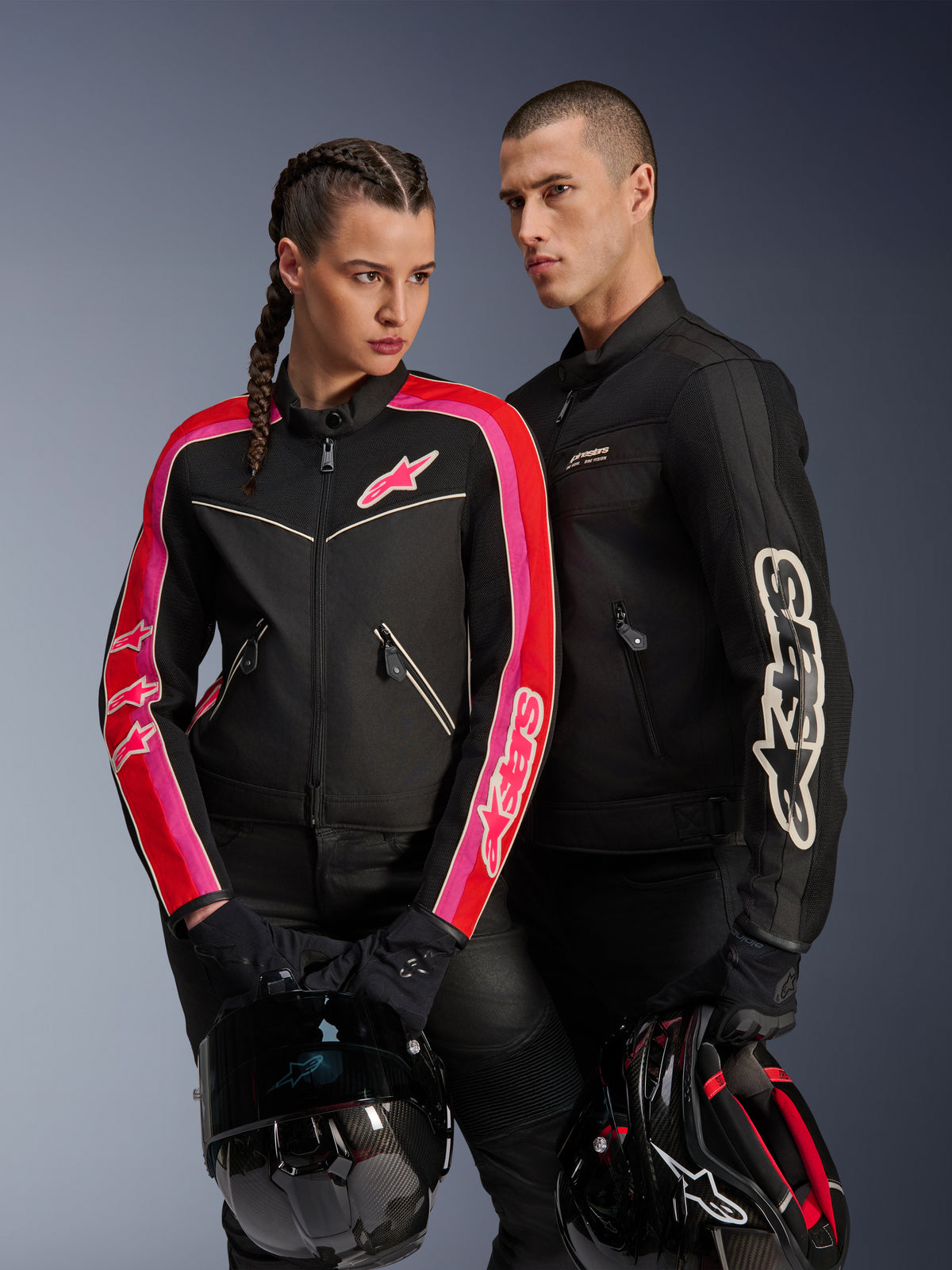 Giacca Alpinestars Stella T-Dyno Air su donna in nero, rosso brillante e fucsia, abbinata alla giacca da uomo Dyno Air nera, entrambi i motociclisti con caschi da moto in mano, scatto in studio di abbigliamento moto urban contemporary