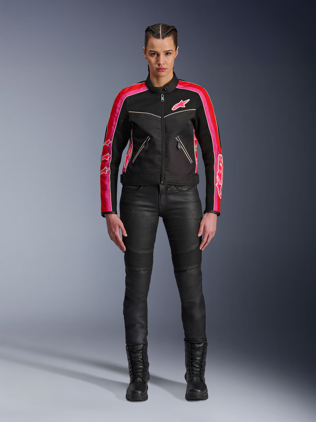 Motociclista che indossa la giacca Alpinestars Stella T-Dyno Air, nera con accenti rosso brillante e fucsia, abbinata a pantaloni da moto neri e stivali stringati, con pannelli in rete 3D, vestibilità su misura e loghi a stella rosa, abbigliamento da moto urban
