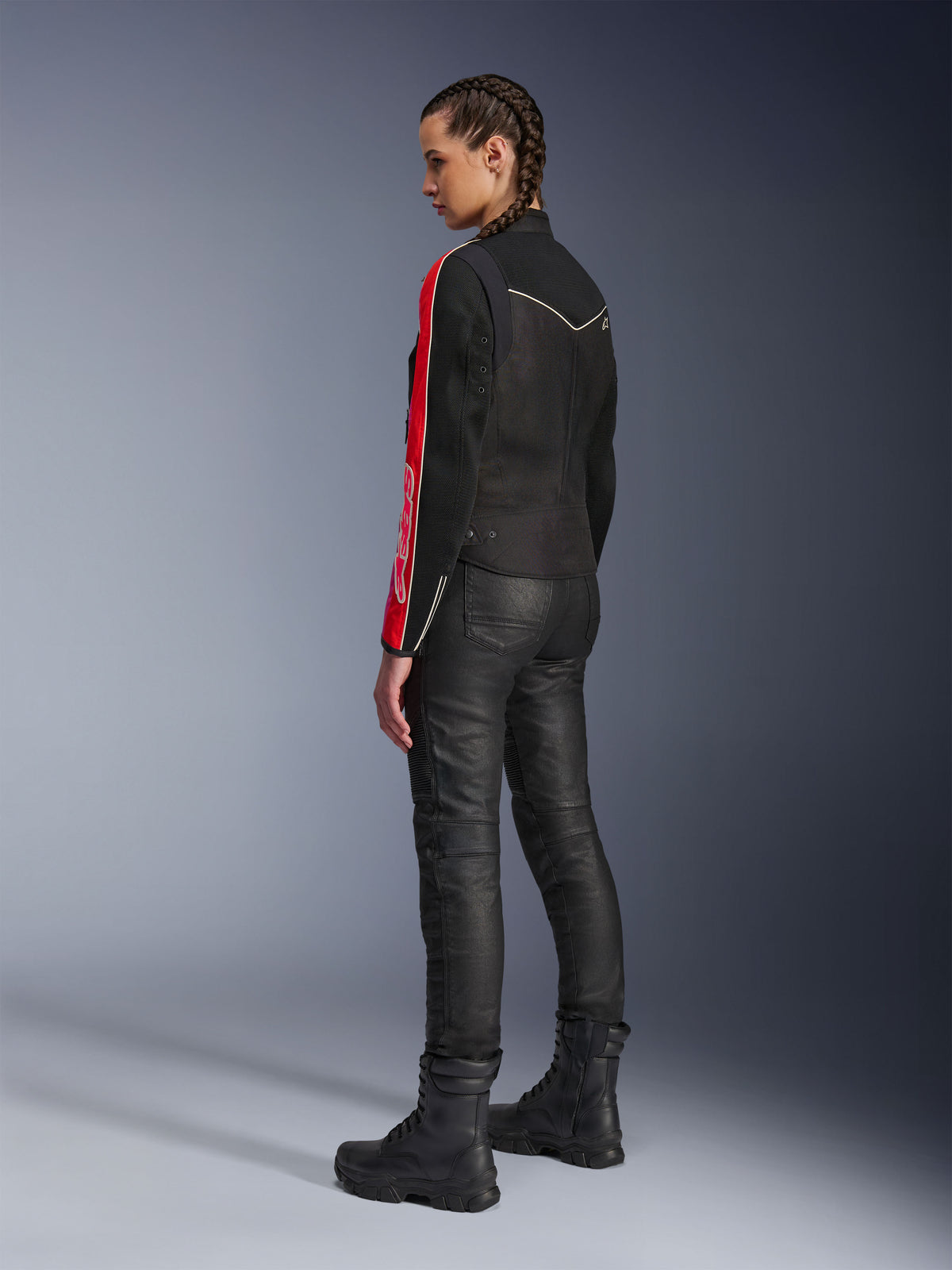 Donna che indossa la giacca Alpinestars Stella T-Dyno Air in Nero Rosso Brillante Fucsia, abbinata a pantaloni da moto neri e stivali neri, vista di profilo che mette in risalto le grafiche rosse e fucsia sulle maniche e la vestibilità da moto su misura.