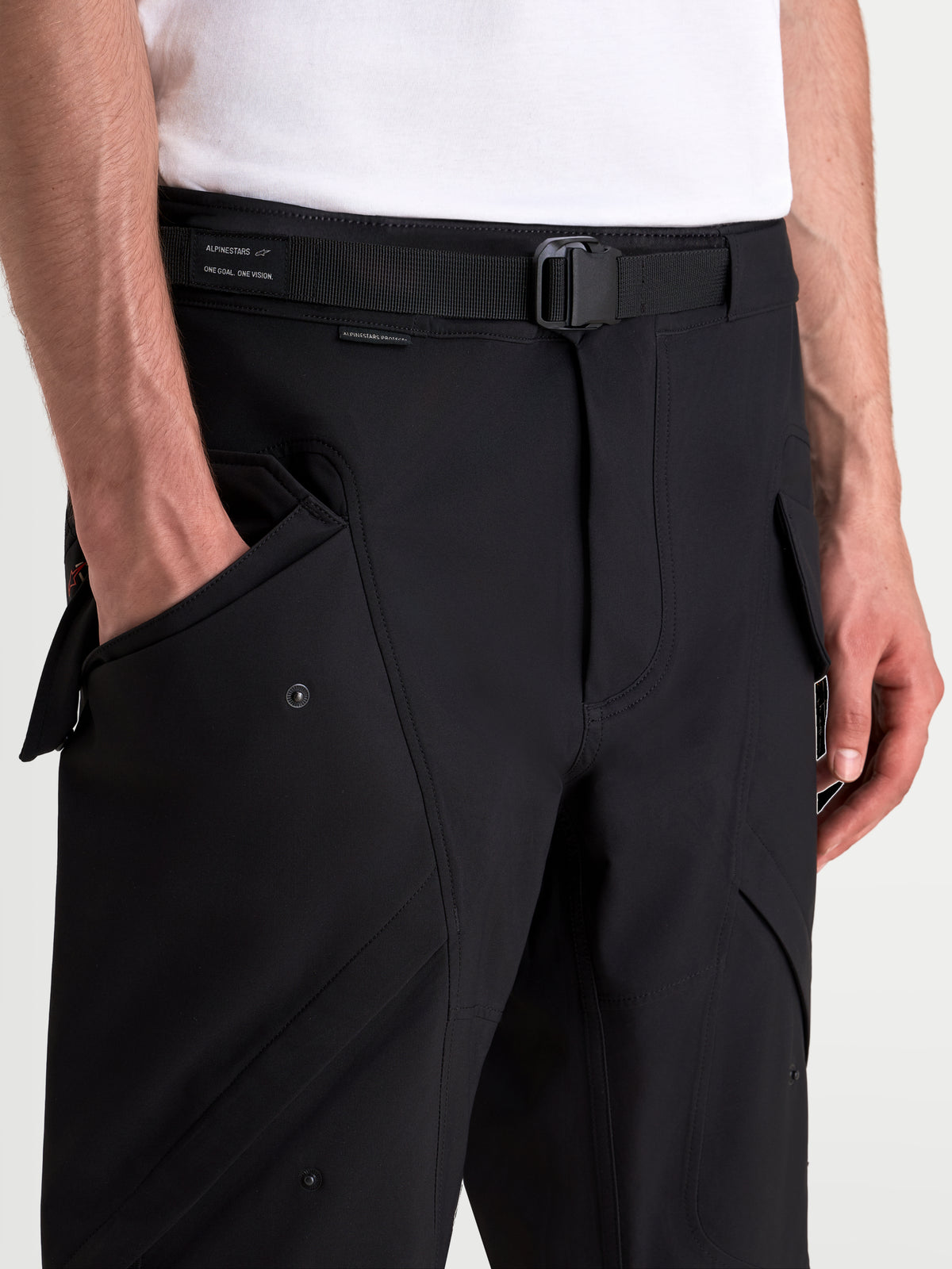 Alpinestars Juggernaut V 2 Drystar Pantaloni, pantaloni da moto urbani neri, vista in primo piano che mostra la cintura regolabile, la fibbia magnetica e le tasche cargo anteriori su un modello