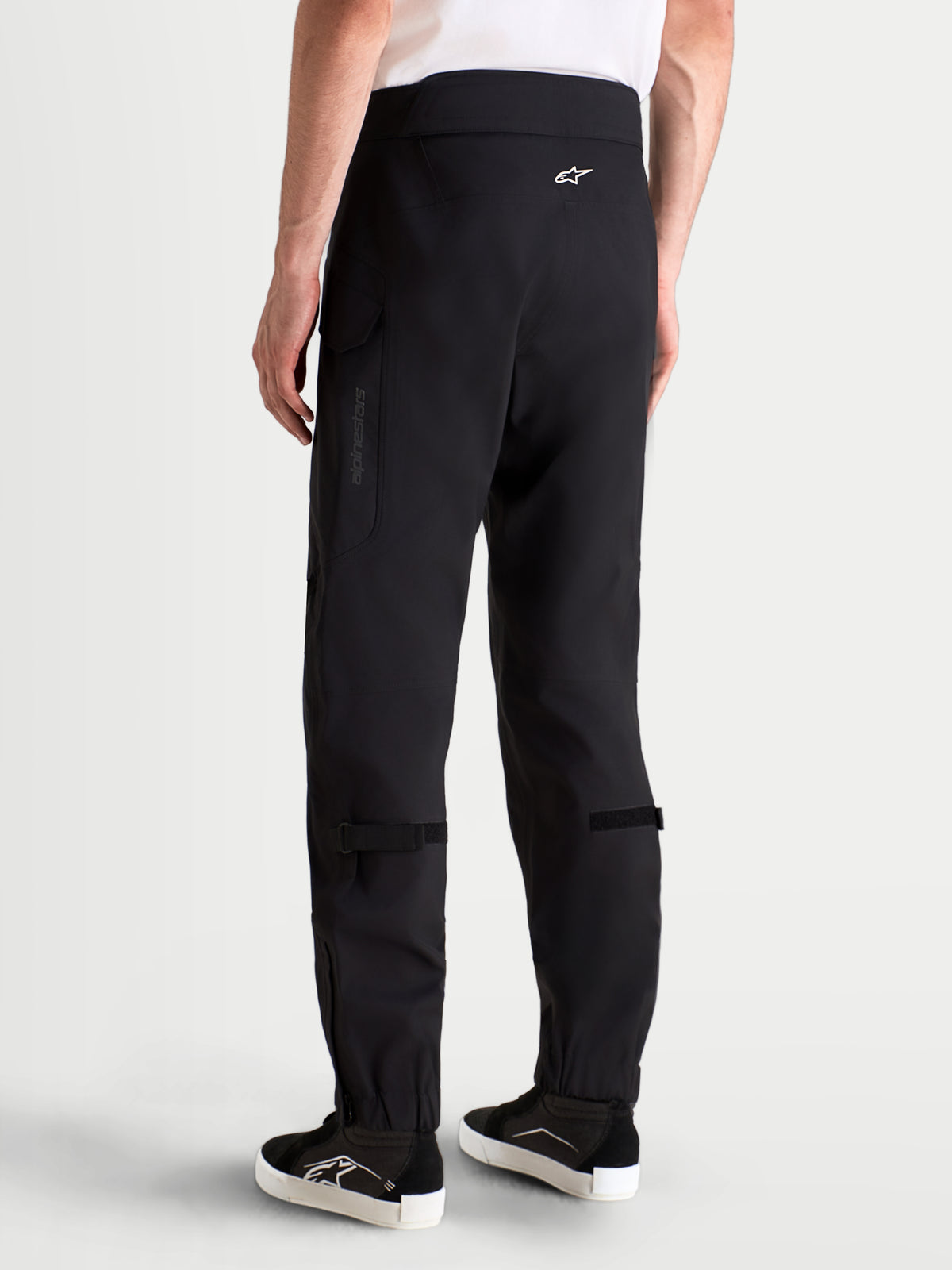 Alpinestars Juggernaut V2 Drystar Pantaloni, pantaloni da moto urbani impermeabili da uomo, colore nero, vista posteriore su un modello con scarpe da moto abbinate, caratterizzati da vita alta e tasche cargo