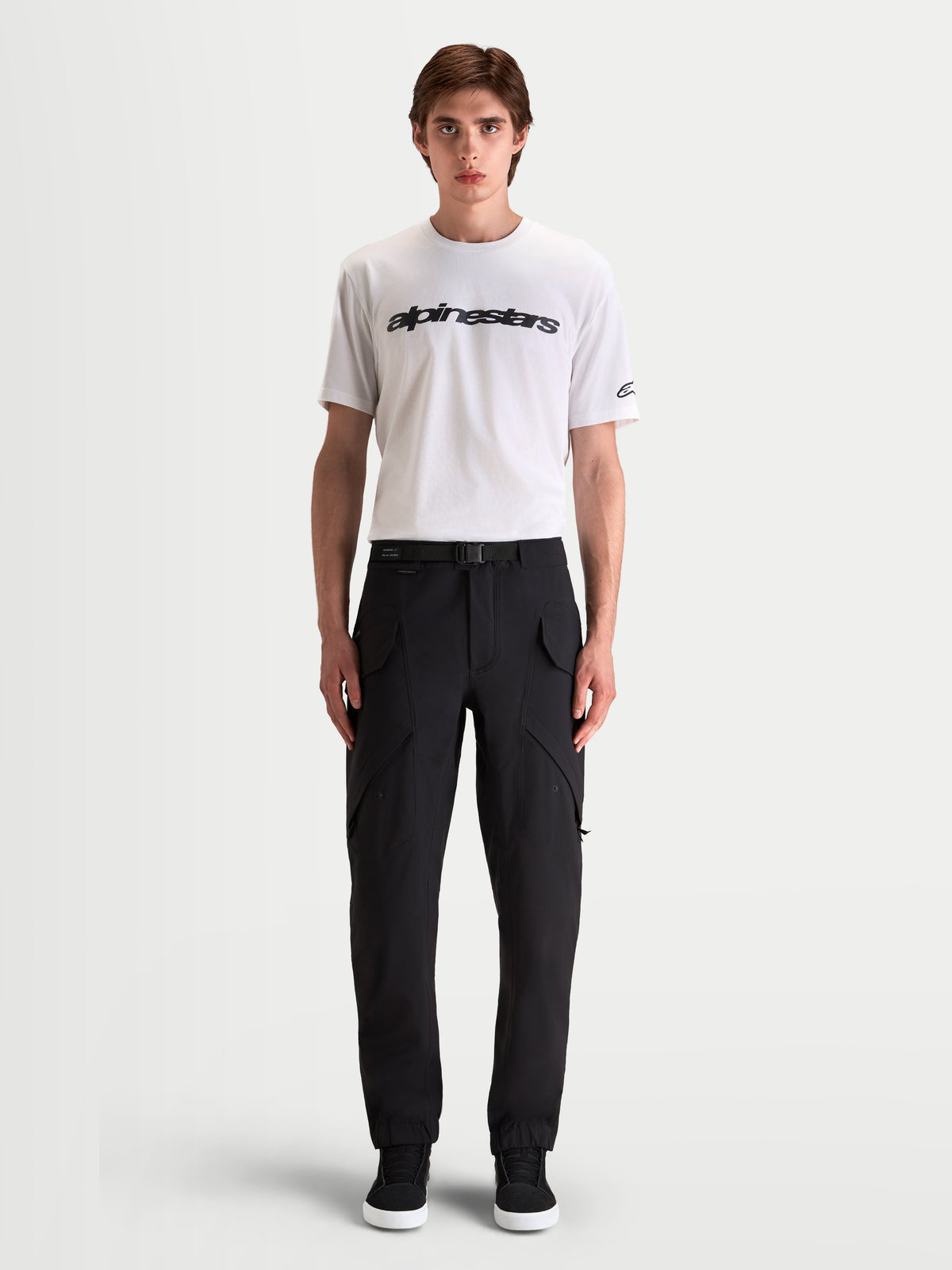 Alpinestars Juggernaut V2 Drystar Pantaloni, pantaloni da moto urbani impermeabili da uomo, colore nero, vista frontale su un modello che indossa una t-shirt bianca e scarpe da moto casual, con tasche cargo multiuso e cintura regolabile in vita