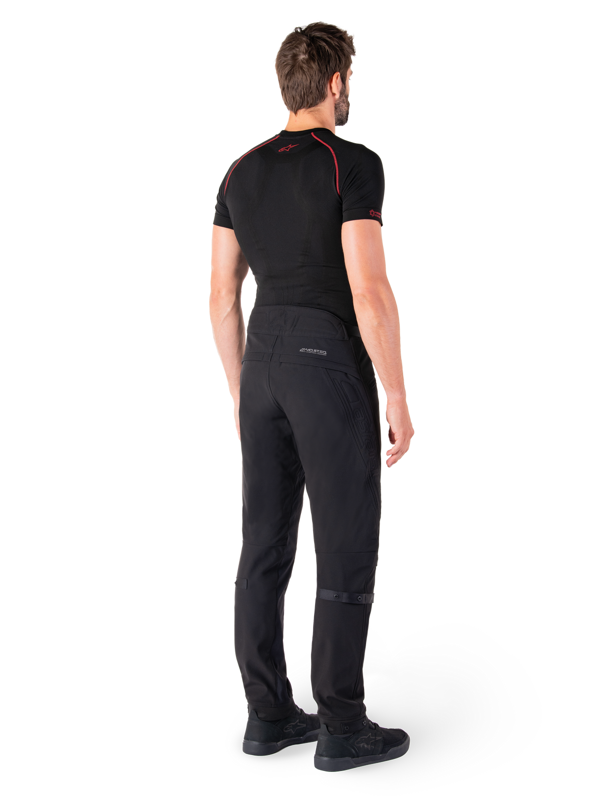 Alpinestars Alden Pants, Nero, pantaloni da moto urban visti dal retro su un modello, indossati con un base layer nero a maniche corte e scarpe da guida nere, caratterizzati da dettagli trapuntati e marchio MO.ST.EQ. riflettente sul carré posteriore.
