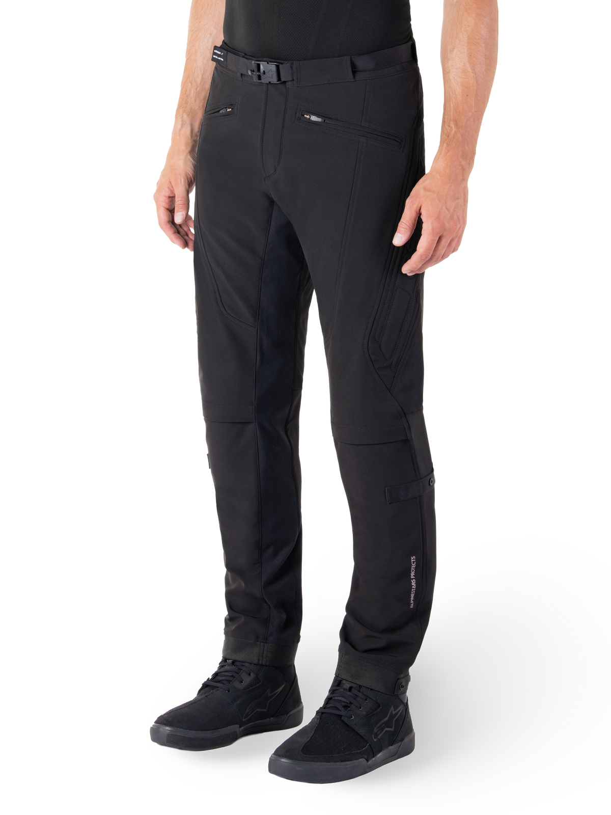Pantaloni Alpinestars Alden, pantaloni da moto urban, nero, tessuto tecnico softshell con vestibilità regolare, caratterizzati da fibbia magnetica in vita, pannelli laterali trapuntati, tasche con zip e logo discreto sulla parte inferiore della gamba, indossati con scarpe da moto nere