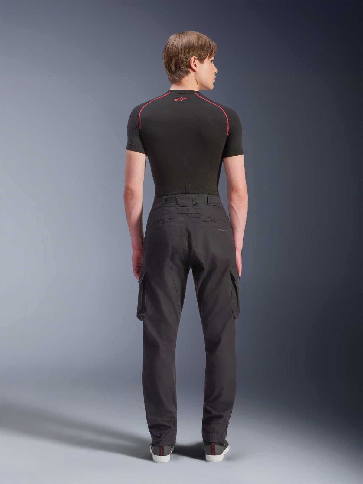 Alpinestars Flex-AST Cargo Pants - Short, nero, pantaloni da moto urbani visti dal retro, con tasche cargo laterali e orli elasticizzati, indossati con un base layer nero a maniche corte con cuciture rosse a contrasto
