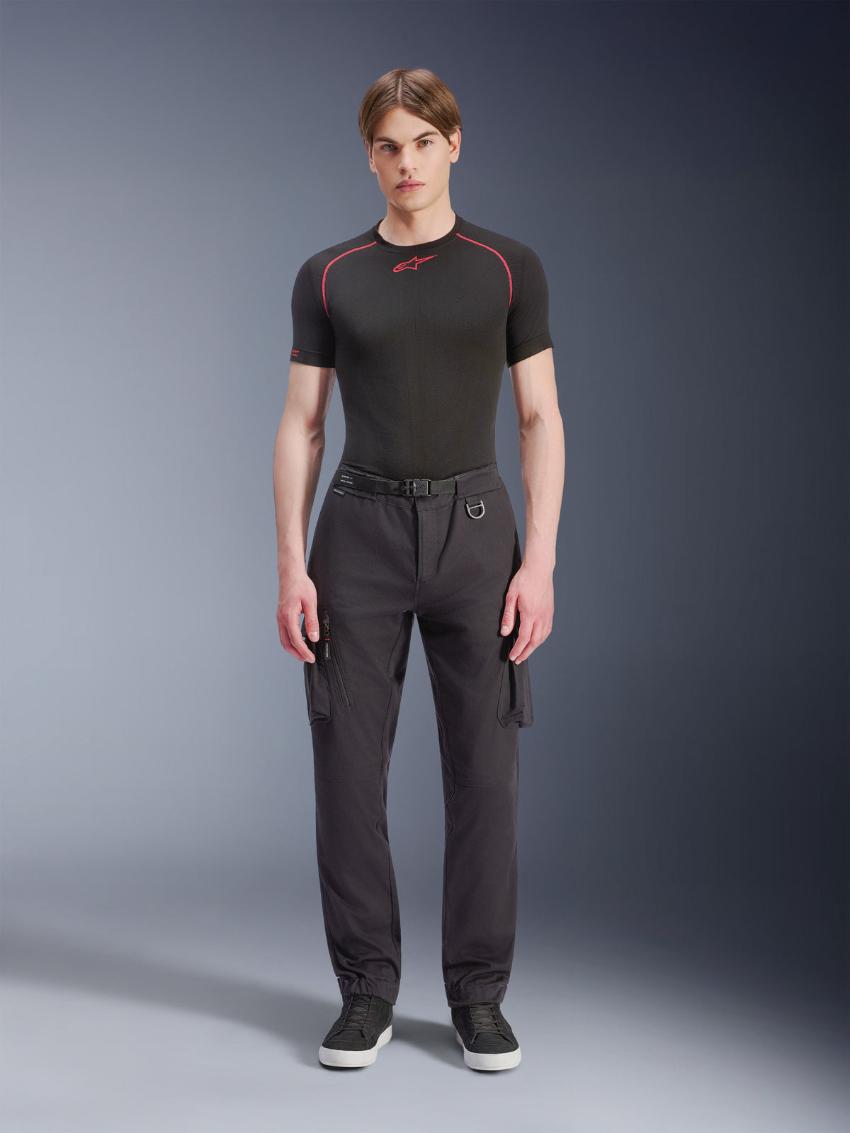 Alpinestars Pantaloni Cargo Flex-AST - Corti, nero, indossati da un modello con una t-shirt tecnica nera e sneakers nere, pantaloni da moto urbani con diverse tasche cargo, vestibilità affusolata e cintura integrata con fibbia e anello a D