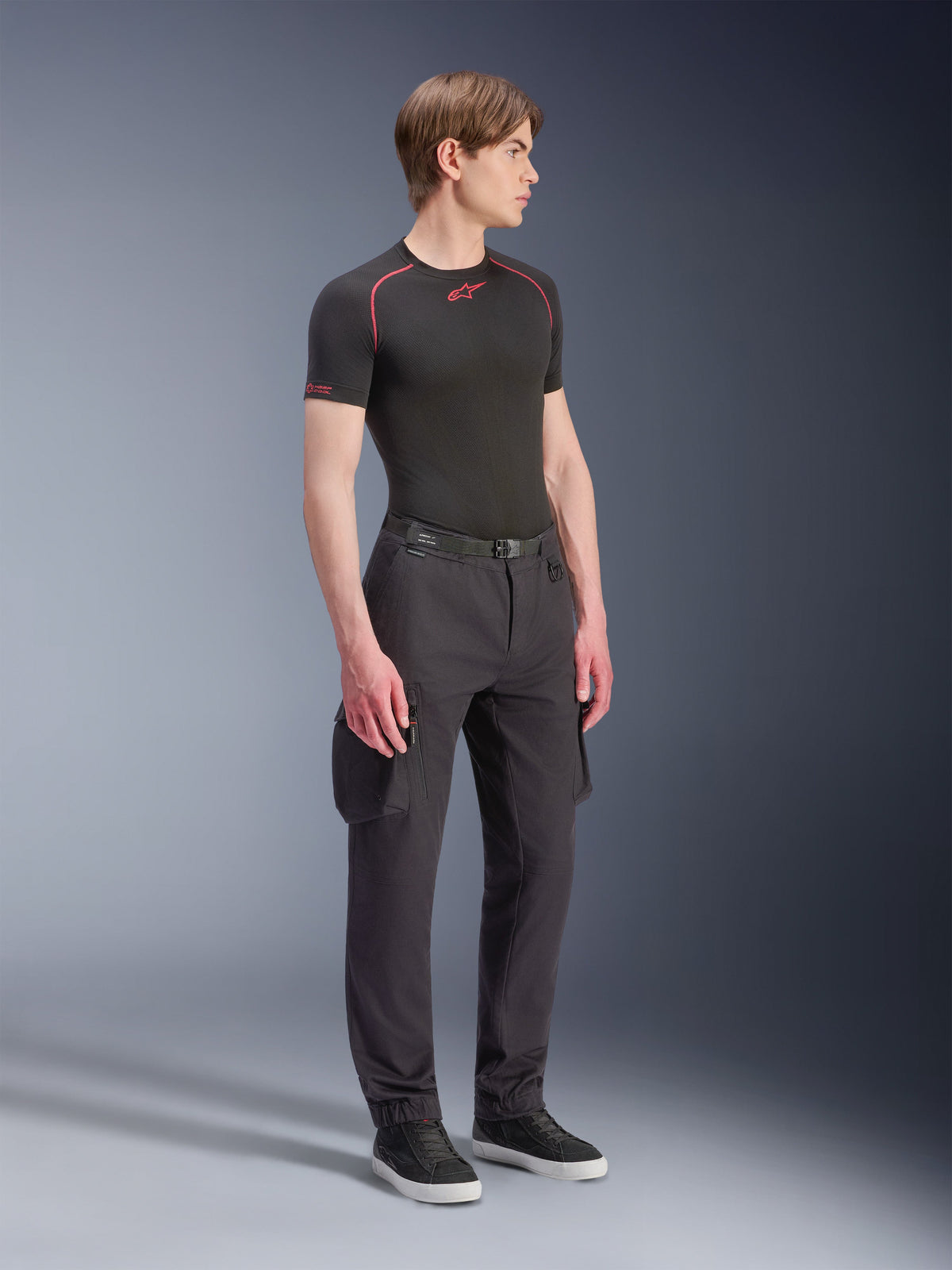 Modello che indossa i pantaloni Alpinestars Flex-AST Cargo - Short in nero, pantaloni cargo da moto urbani con tasche laterali e gambe affusolate, abbinati a un base layer nero e sneakers, abbigliamento da moto urbano.