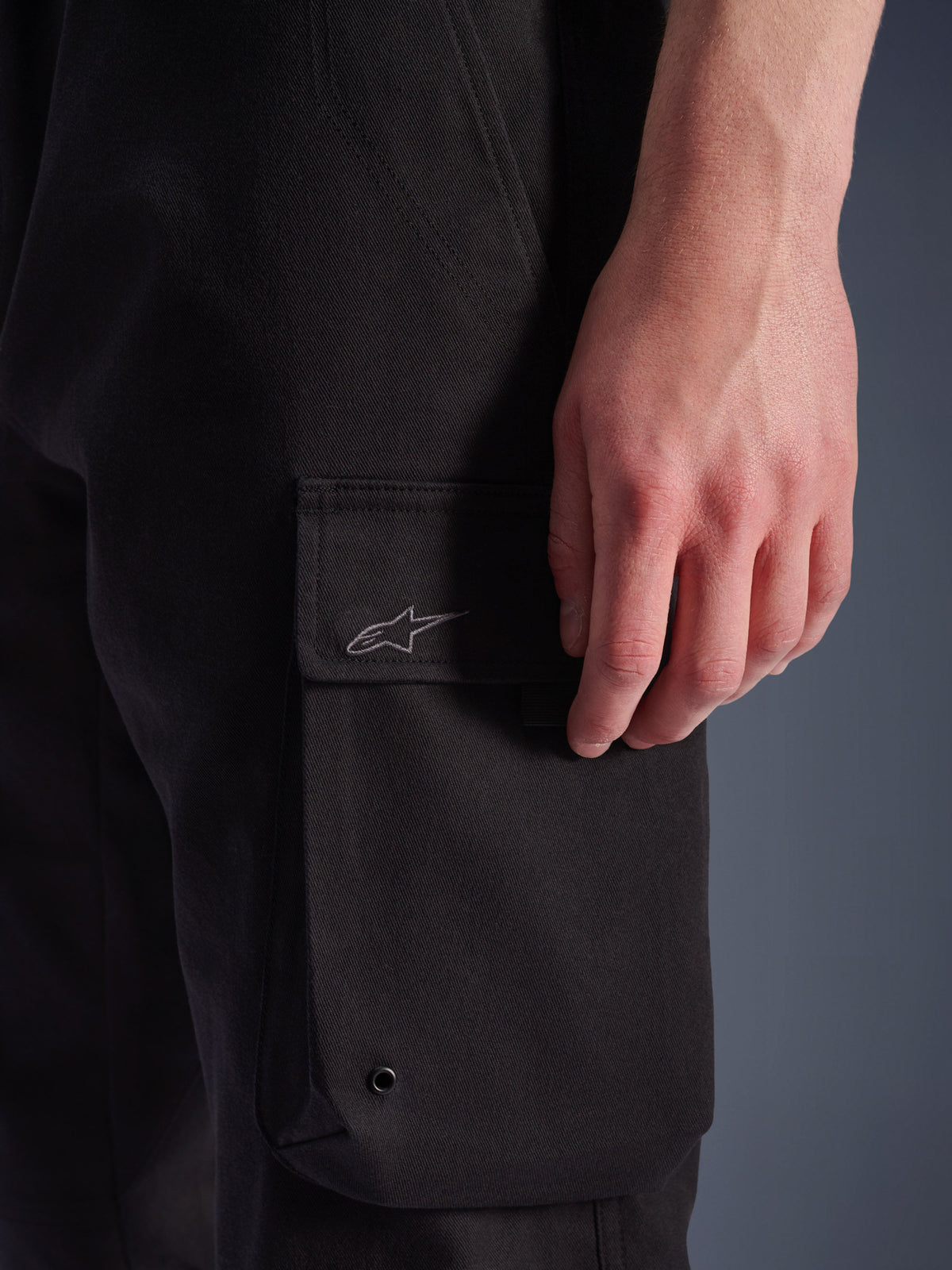 Alpinestars Flex-AST Cargo Pants, pantaloni da moto urban, nero, primo piano della tasca cargo laterale con logo Astar ricamato, occhiello in metallo e trama in twill elasticizzato resistente
