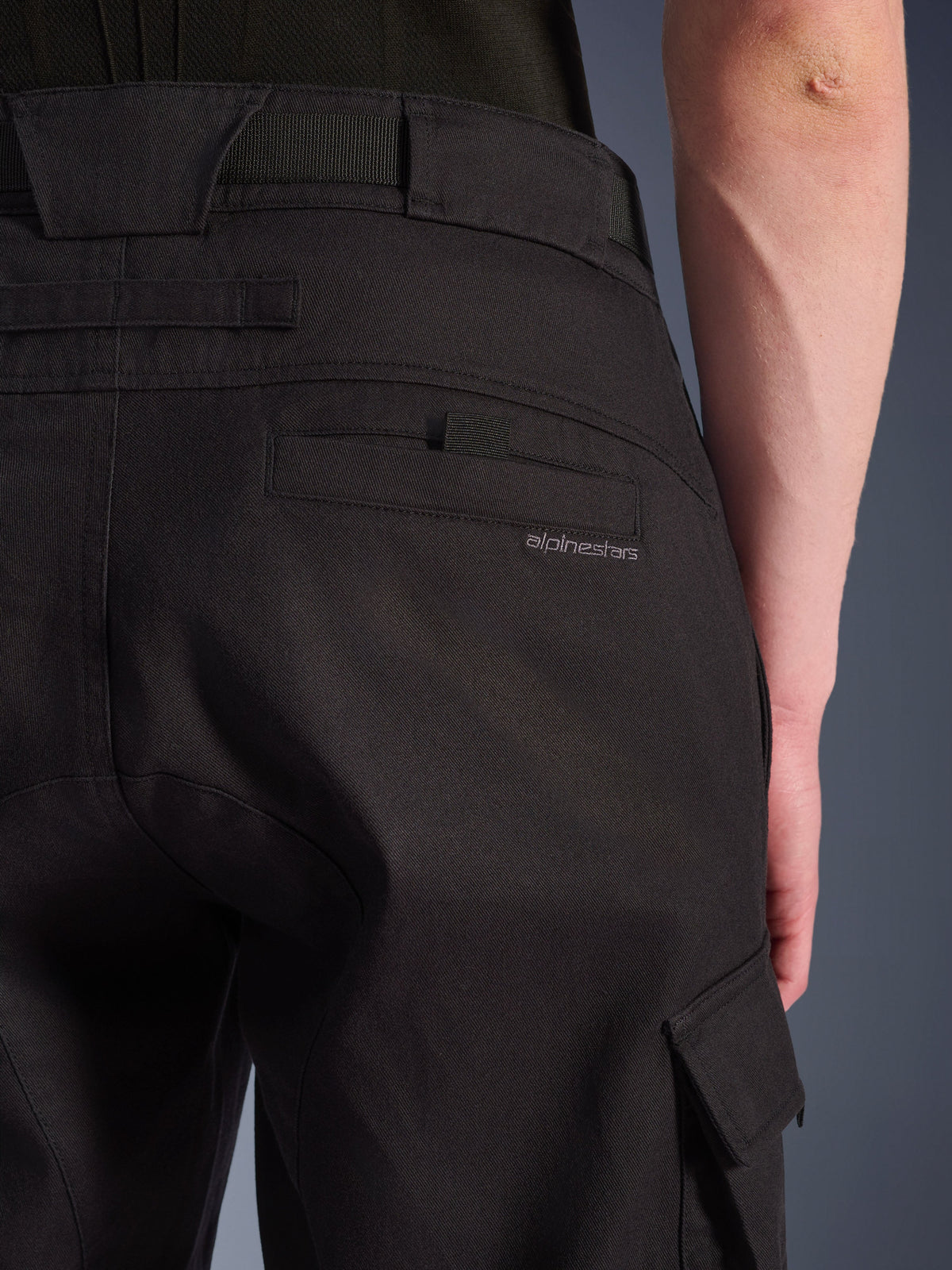 Primo piano dei pantaloni cargo Alpinestars Flex-AST neri, pantaloni da moto urbani con tasca posteriore dettagliata e marchio discreto, ampi passanti per cintura e tasca cargo laterale in tessuto elasticizzato resistente.
