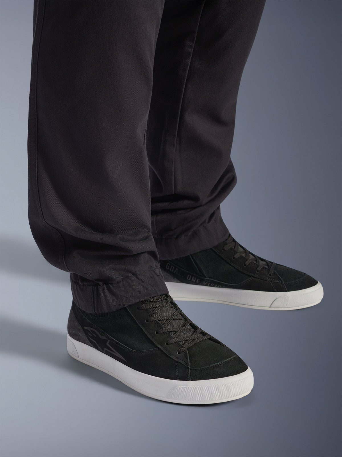 Alpinestars Flex-AST Cargo Pants - Short, pantaloni da moto urbani neri, caratterizzati da gambe affusolate con orli elasticizzati, abbinati a sneakers Alpinestars nere, stile di guida urbano contemporaneo