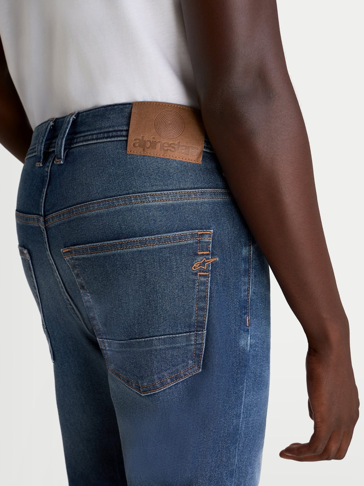 Alpinestars Flex Ast 8 Denim Pantaloni, jeans da moto urban da uomo, blu medio, vista posteriore che mostra la toppa posteriore in pelle, le cuciture a contrasto e il logo Astar ricamato sulla tasca indossati da un modello