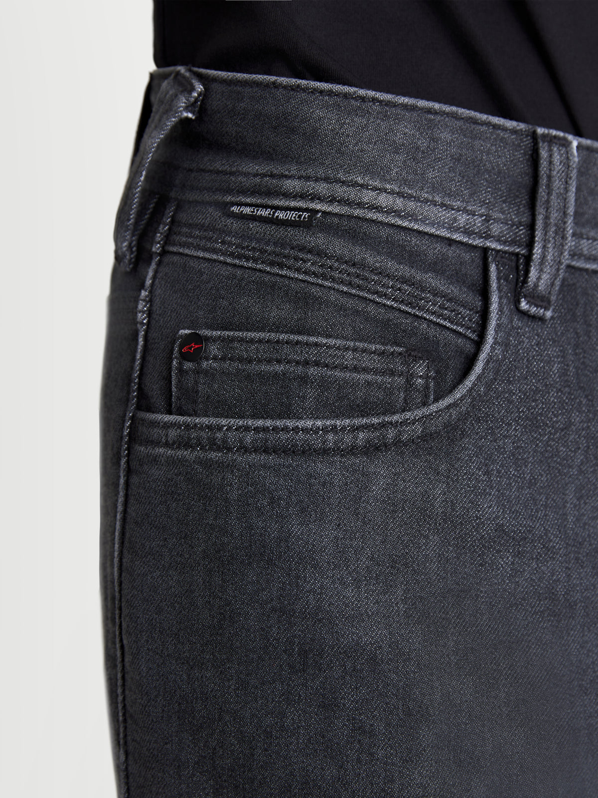 Alpinestars Flex-AST 7 Denim Pantaloni, jeans da moto urban da uomo in nero slavato, vista in primo piano che mostra la costruzione delle tasche, il dettaglio del rivetto logato e l'etichetta tessuta Alpinestars Protects