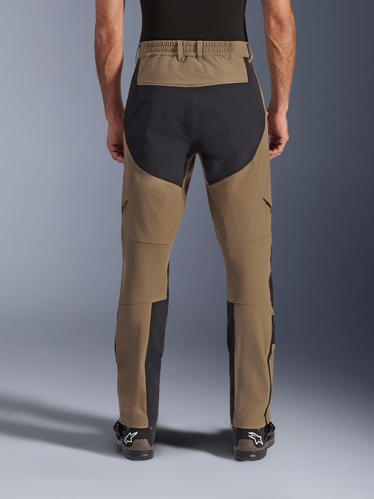 Pantaloni Alpinestars Flex-AST Explorer, pantaloni da moto adventure, Walnut Black, vista posteriore indossata dal pilota, pannelli di rinforzo in ripstop nero sulla seduta e sull'interno gamba, vita elasticizzata, lunghe cerniere sulla parte inferiore della gamba e stivali adventure coordinati