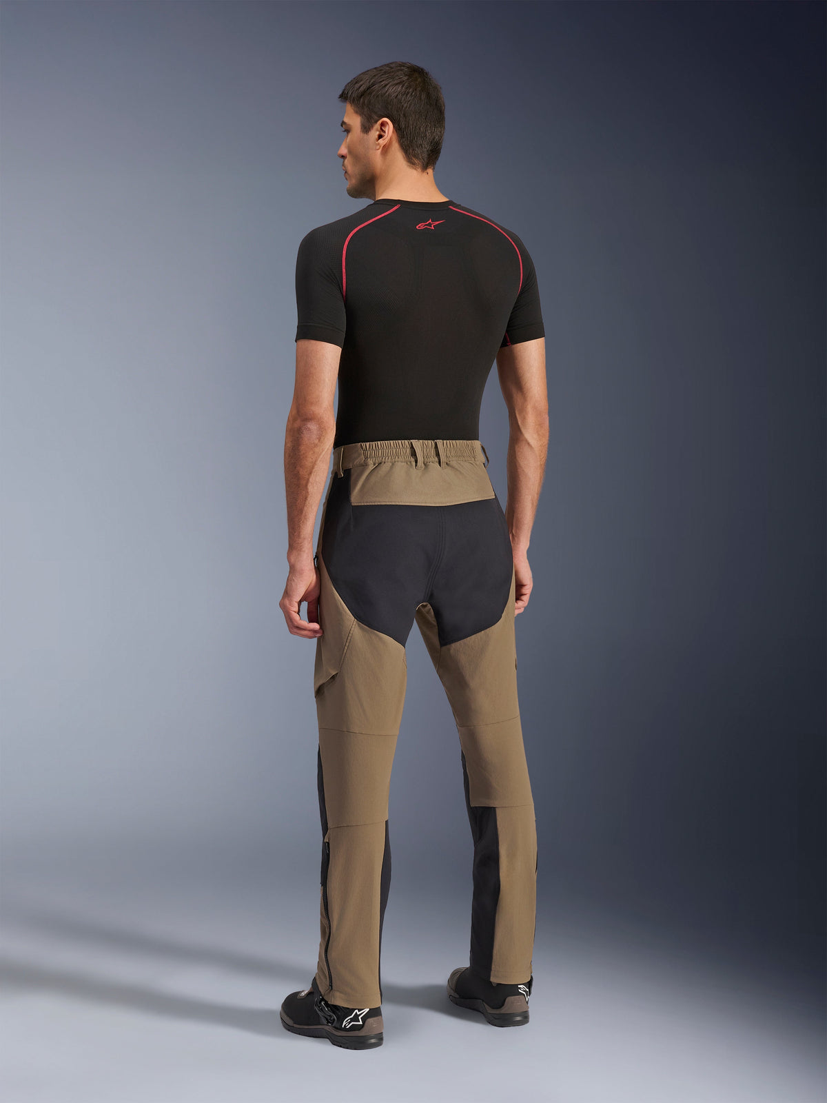 Pantaloni Alpinestars Flex-AST Explorer, pantaloni da moto adventure, Walnut Black, vista posteriore su modello con pannelli neri in ripstop su seduta e gambe, costruzione in tessuto elasticizzato e lunghe cerniere a fondo gamba per l'adventure touring
