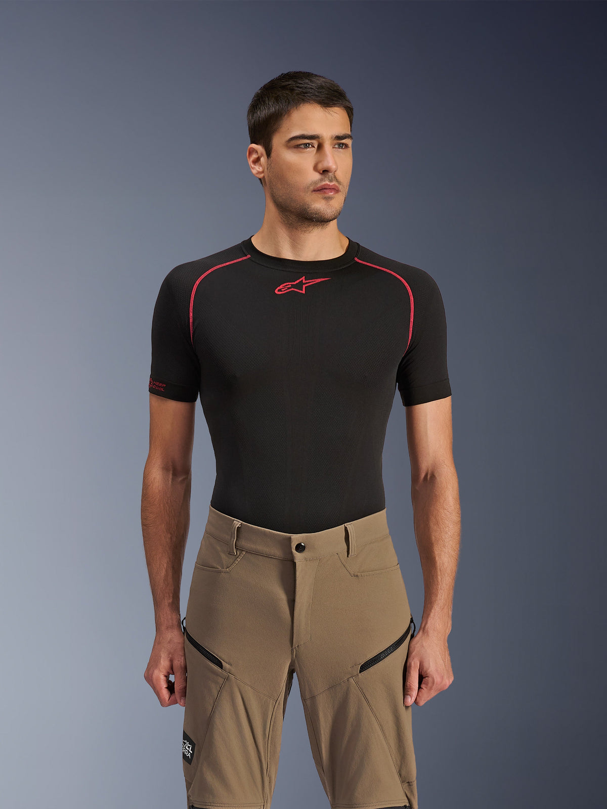 Pantaloni Alpinestars Flex-AST Explorer, pantaloni da moto adventure, Walnut Black, indossati da un modello con una maglia base layer nera, con tasche cargo diagonali con cerniera e costruzione in tessuto elasticizzato resistente.