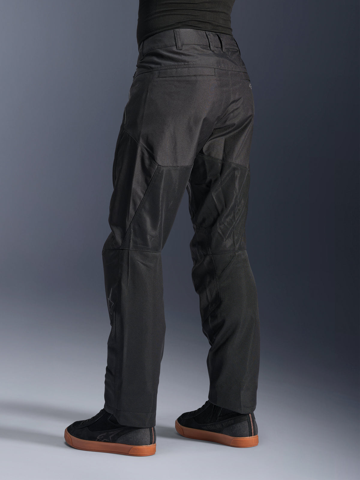 Alpinestars C-1 Air Pants, pantaloni da moto urban, nero, vista posteriore che mostra ampi pannelli in mesh tecnico sulla parte posteriore delle gambe per la ventilazione, design pulito per la guida in città, indossati con sneaker casual nere.