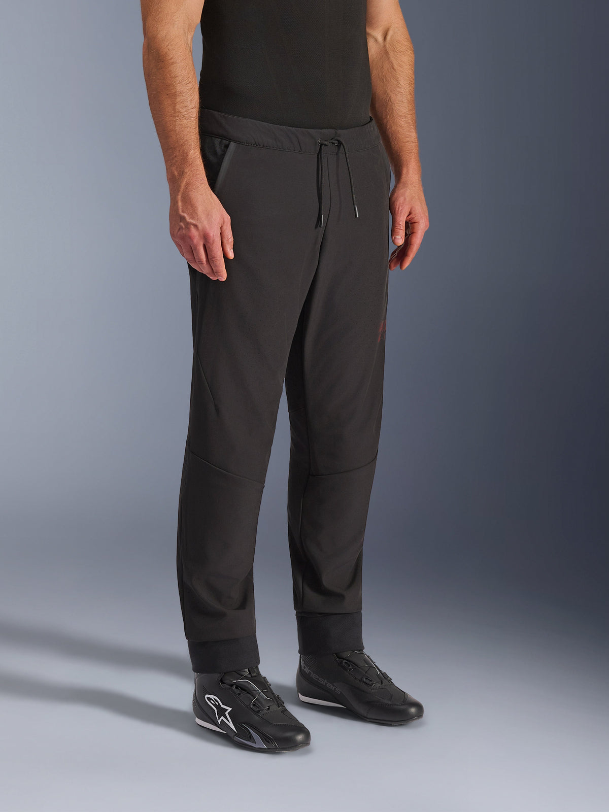 Pantaloni Alpinestars Aeroshell Airflow, pantaloni da moto neri, indossati con scarpe da guida nere, con vita a coulisse, polsini alle caviglie e tessuto softshell perforato al laser per la massima ventilazione